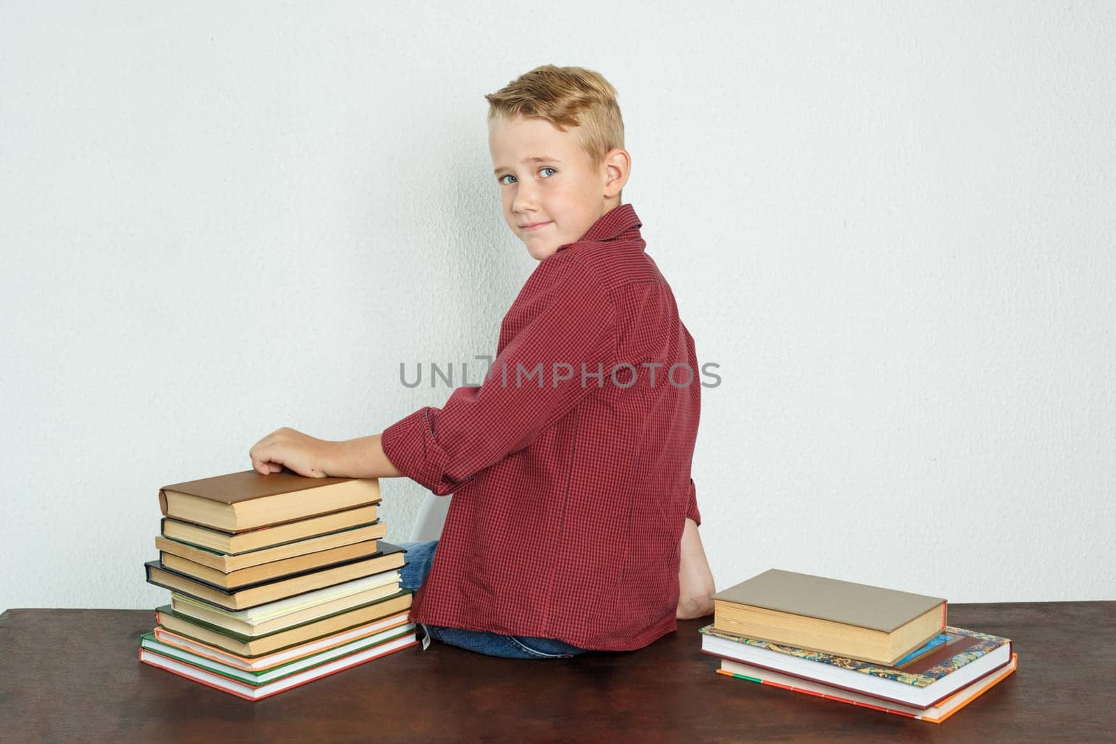 Education concept. A student boy sits on a table with his back to the camera, turned his head to the camera looking at her.