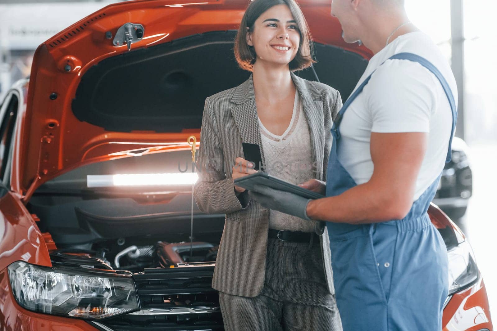 Paying for service. Man repairing woman's automobile indoors.