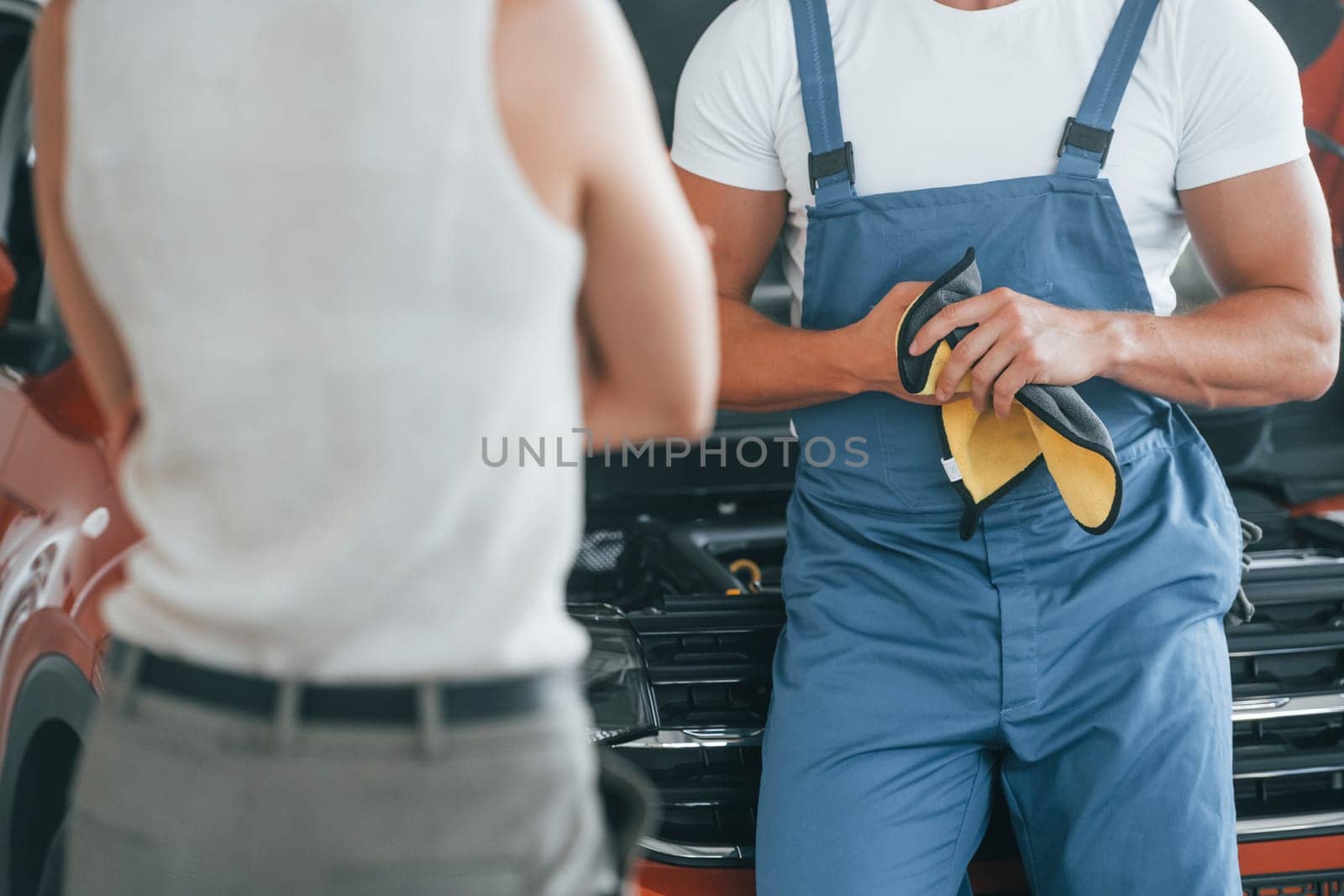 Cropped photo. Man repairing woman's automobile indoors. Professional service.
