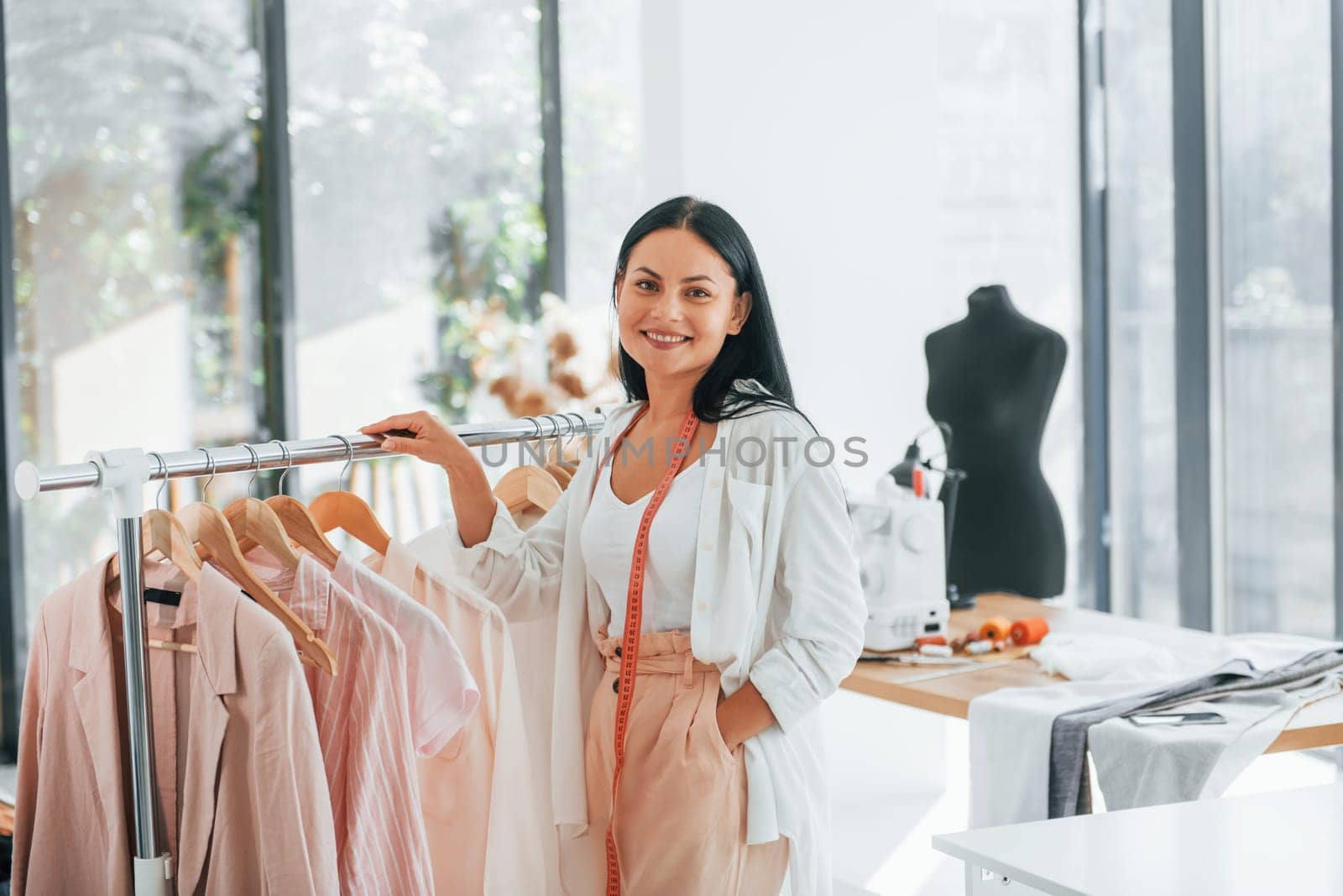 Standing and smiling. Seamstress is in her office that is with different clothes.