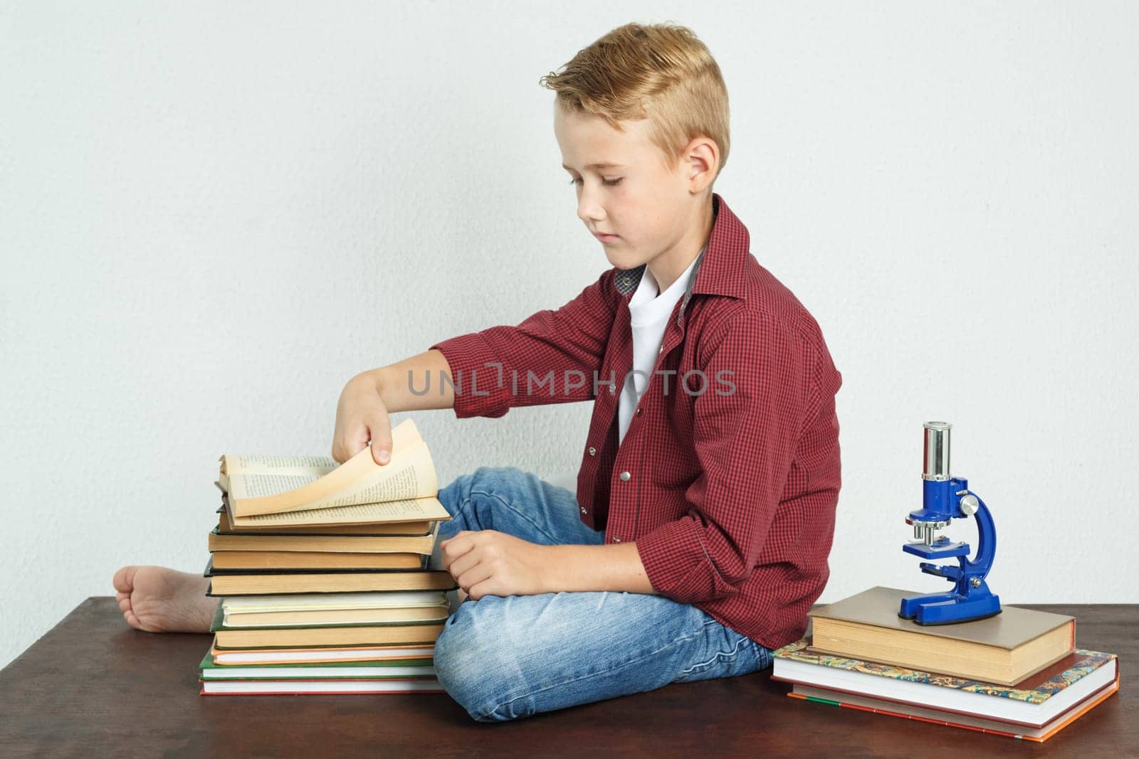 Schoolboy sitting at the table near the books and leafing through the pages of the book. by Sd28DimoN_1976