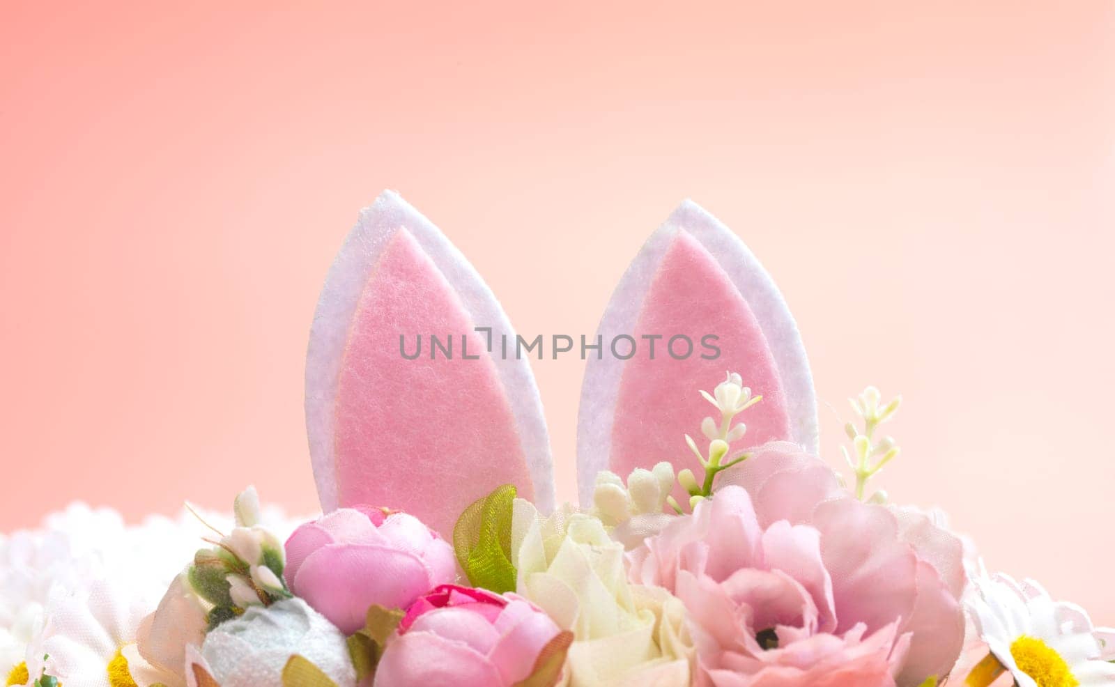 Spring holidays creative background with bunny ears decorated with bloom flowers on pastel pink theme. Creative copy space Easter concept space for text