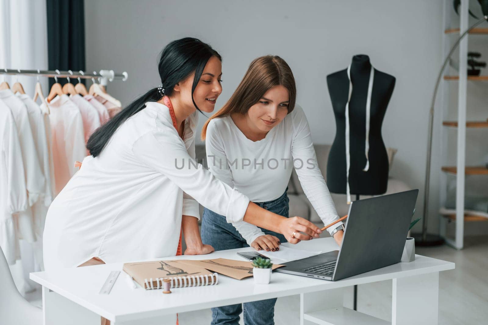 Talking with female customer. Seamstress is in her office that is with different clothes.