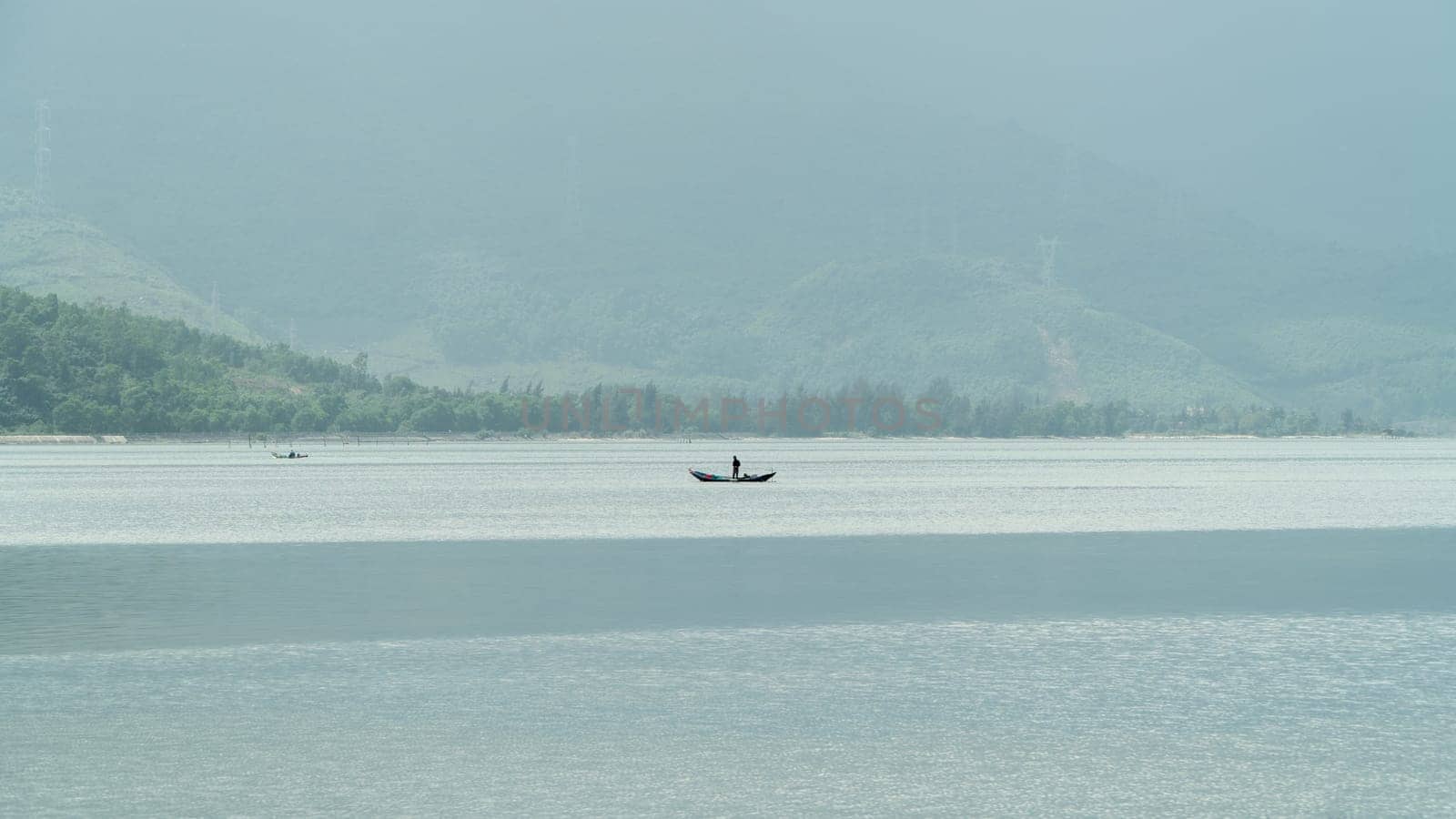 A boat with a fisherman in the middle of the river against the backdrop of foggy mountains. High quality photo