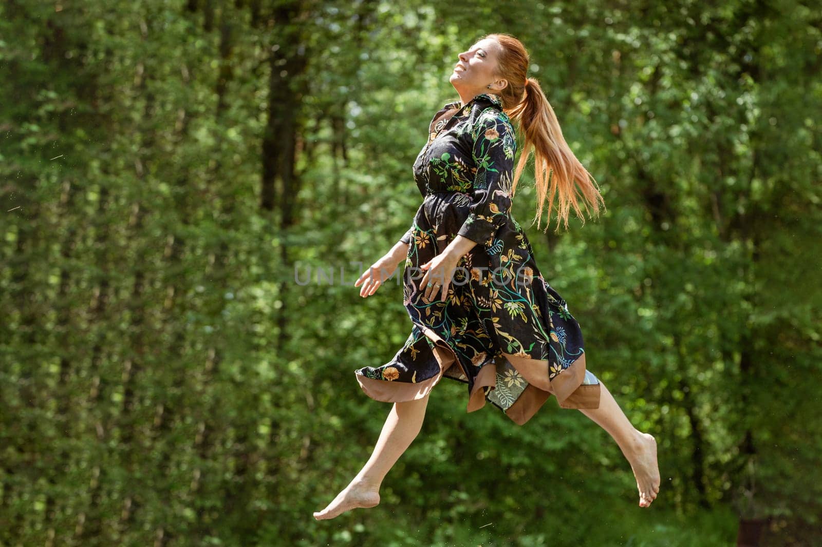 Beautiful happy woman jumps on trampoline outdoor at summer. by EkaterinaPereslavtseva