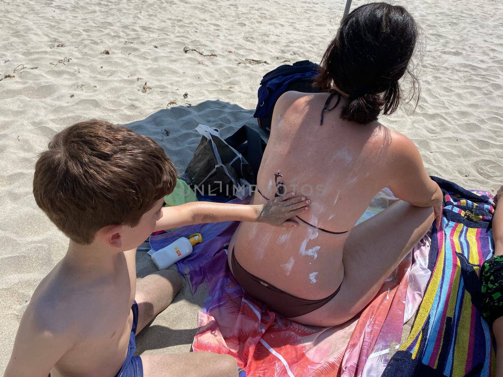 Smiling young boy applying sunscreen on his mother shoulder in the beach