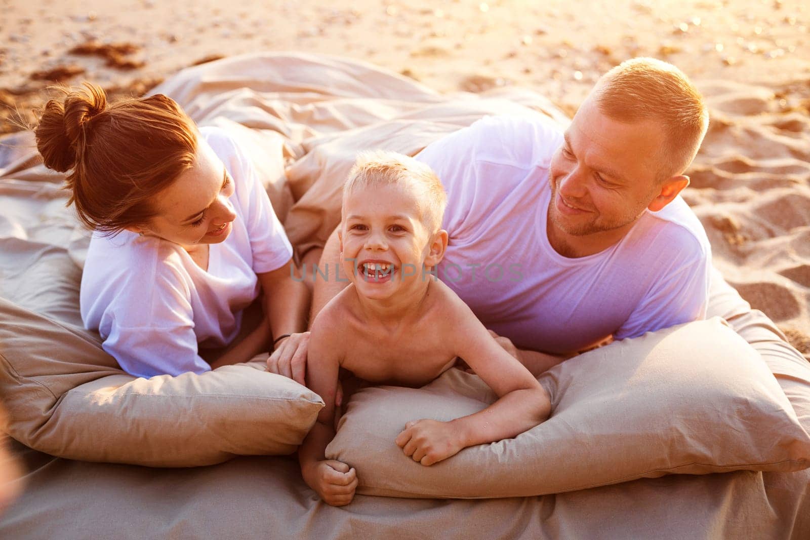 Family vacation by the sea. Happy young caucasian family resting together at sunset. A bed on the sand on a bed of the ocean in the rays of the setting sun