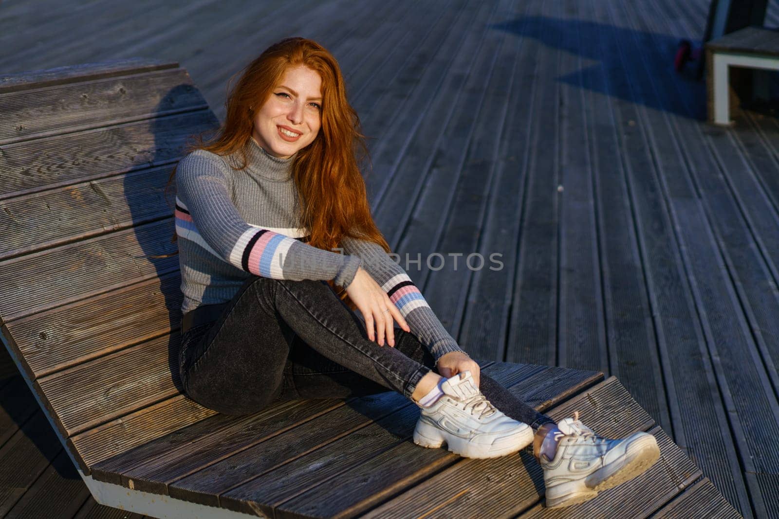 Happy young woman with red hair in the park on wooden flooring by EkaterinaPereslavtseva