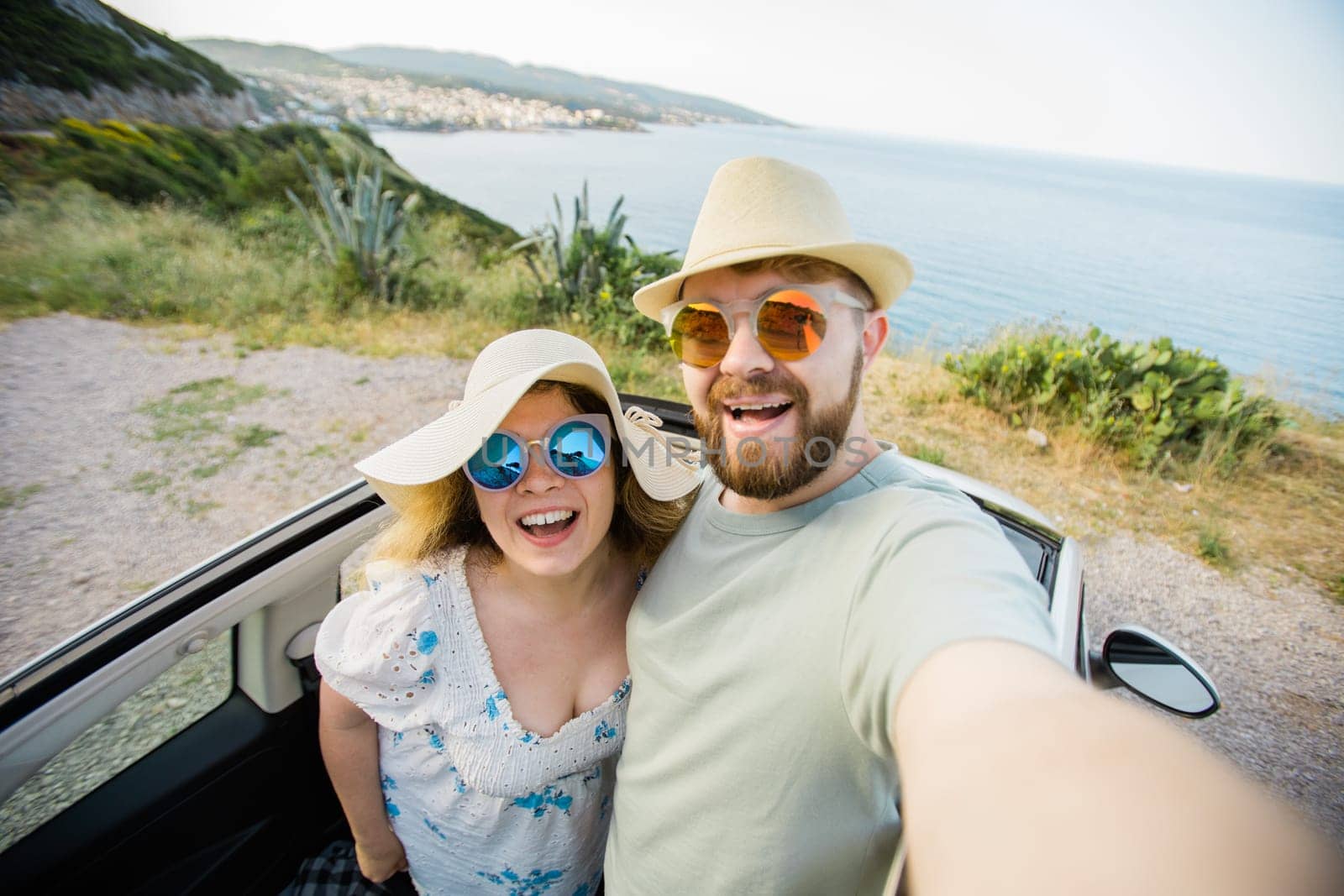 Happy beautiful couple in love taking a selfie portrait driving a convertible car on the road at vacation. Rental cars and vacation concept