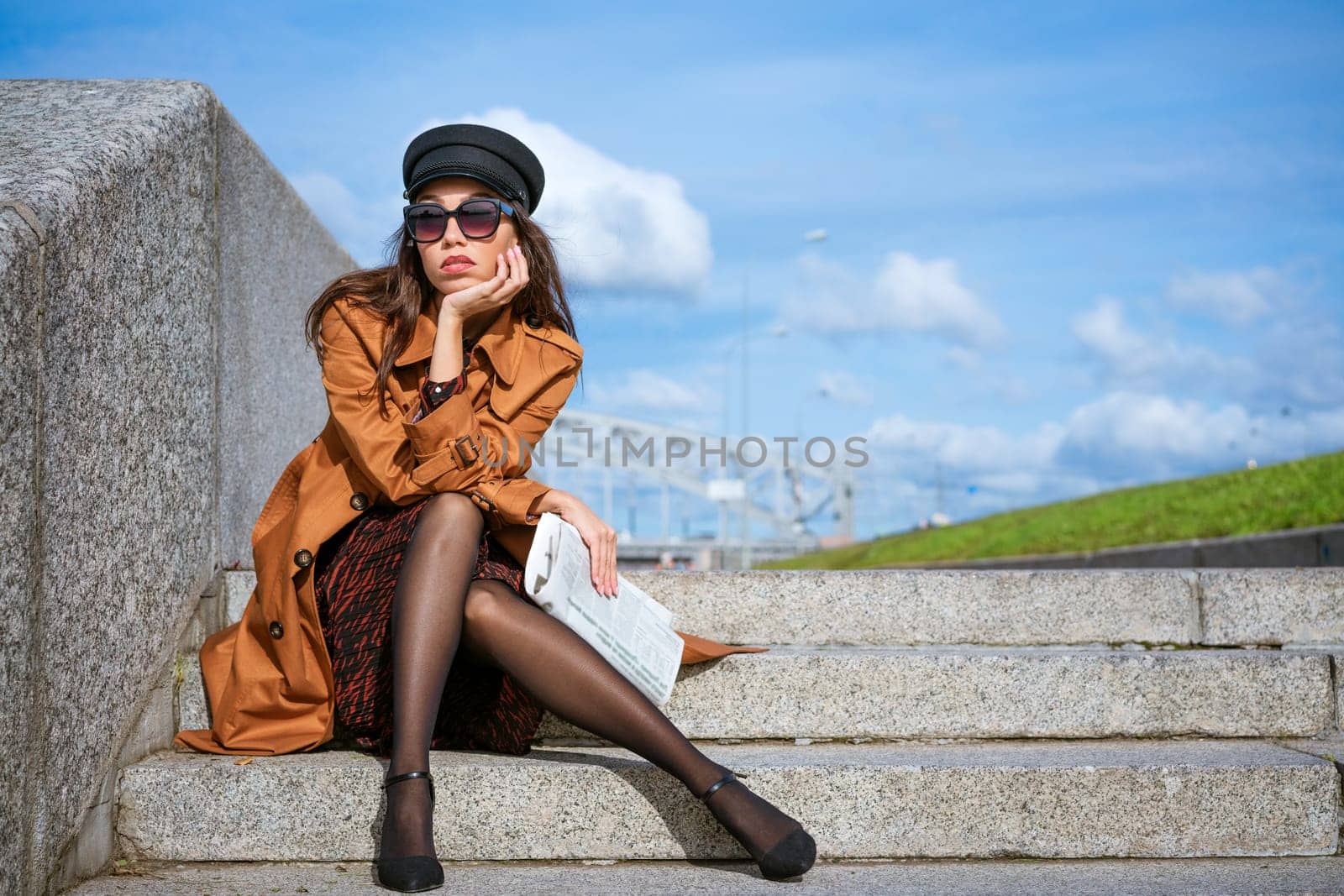 Young woman sits on the steps on the embankment with newspaper in hand by EkaterinaPereslavtseva