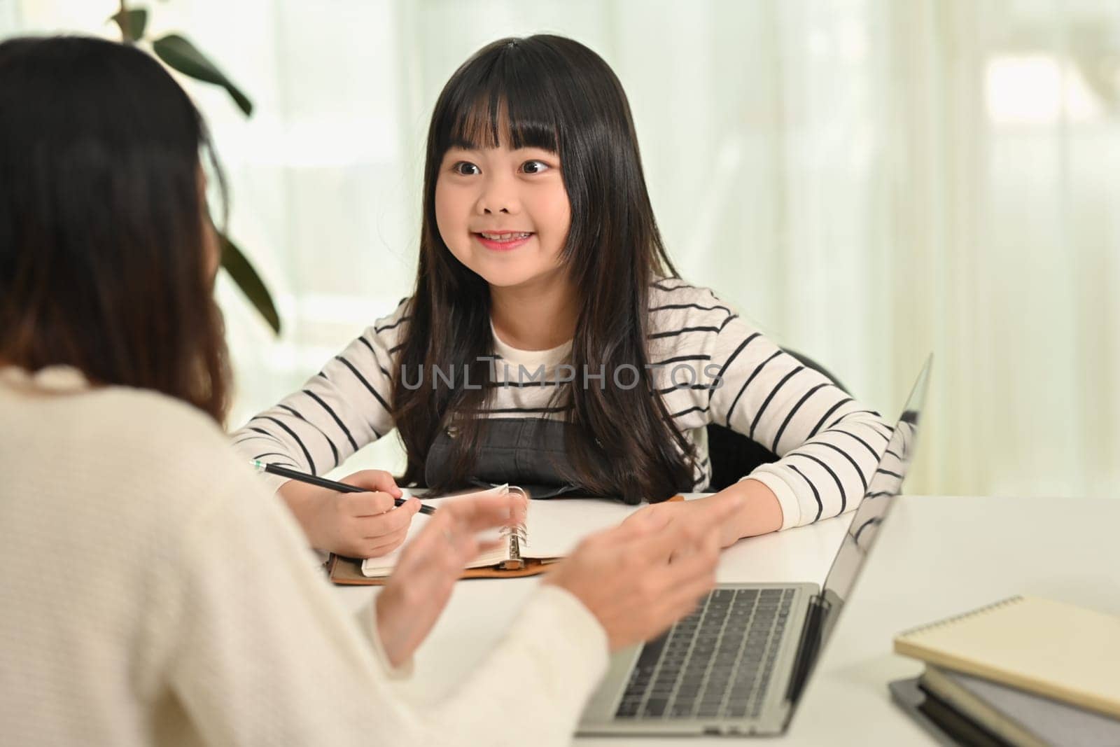 Interested happy little Asian girl doing home working with tutor or mother at home. Homeschooling and learning concept by prathanchorruangsak