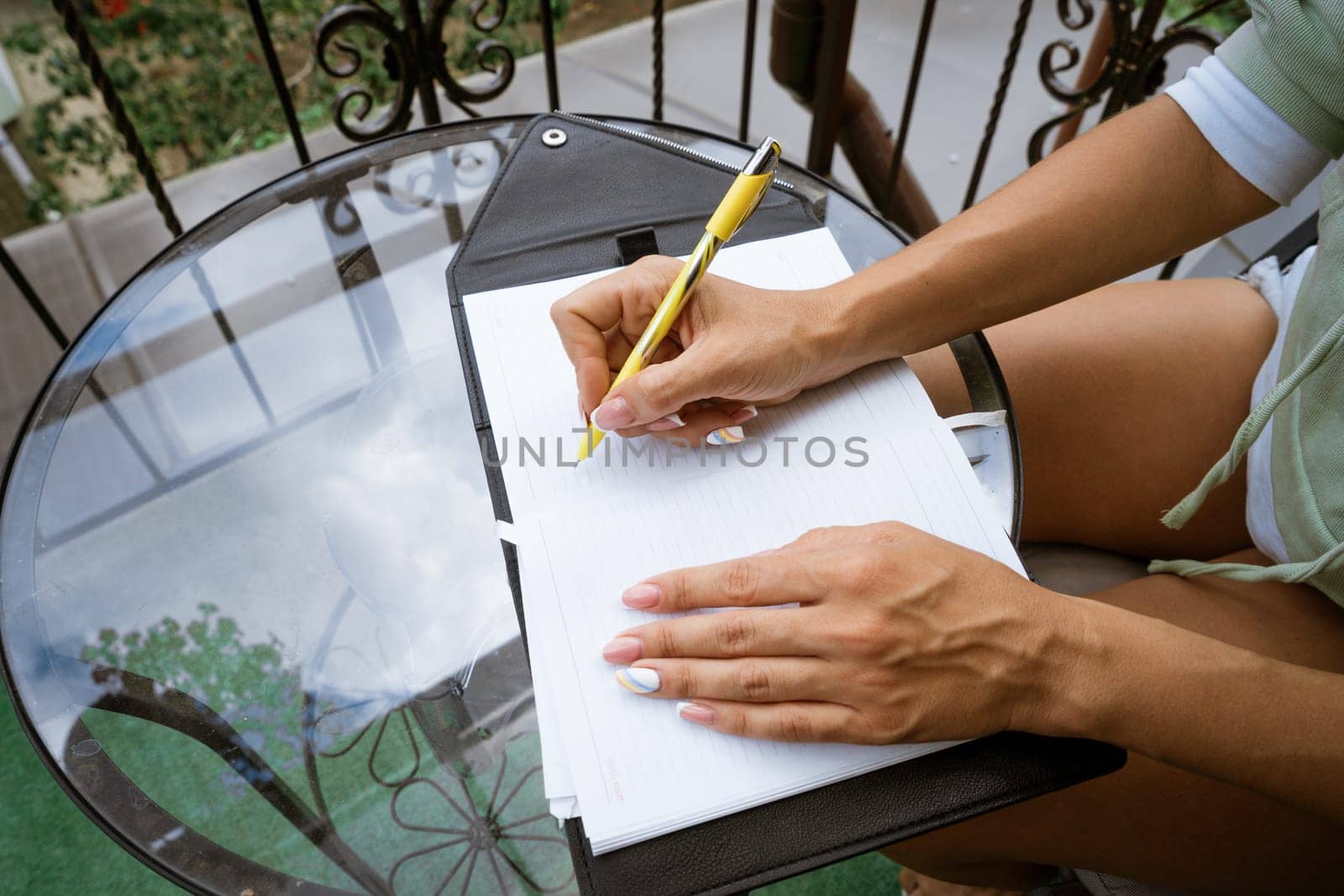 woman writes in a notebook with a pen while sitting at the table at home on the terrace