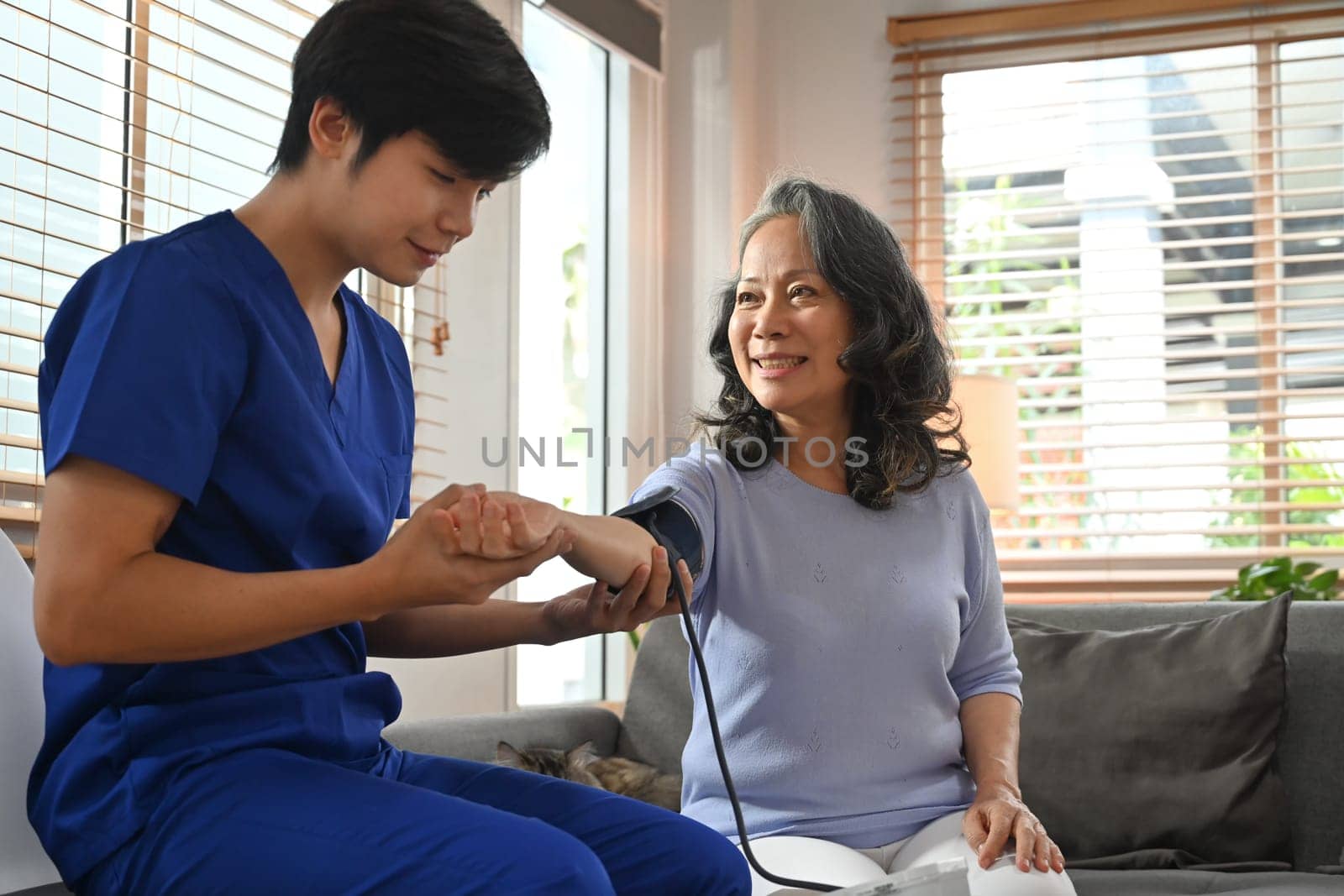 Young male healthcare worker measuring blood pressure middle age woman during home visit. Home health care service concept.
