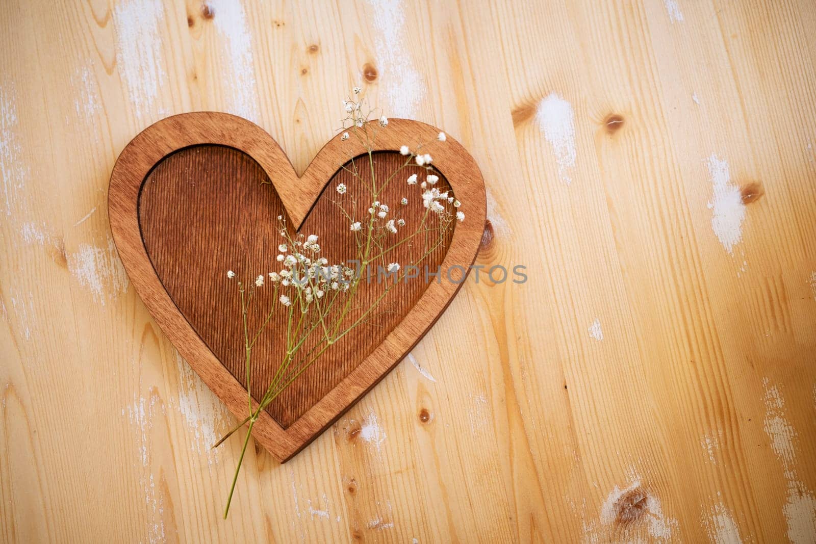 wooden heart with a sprig of small white flowers lies on a wooden background