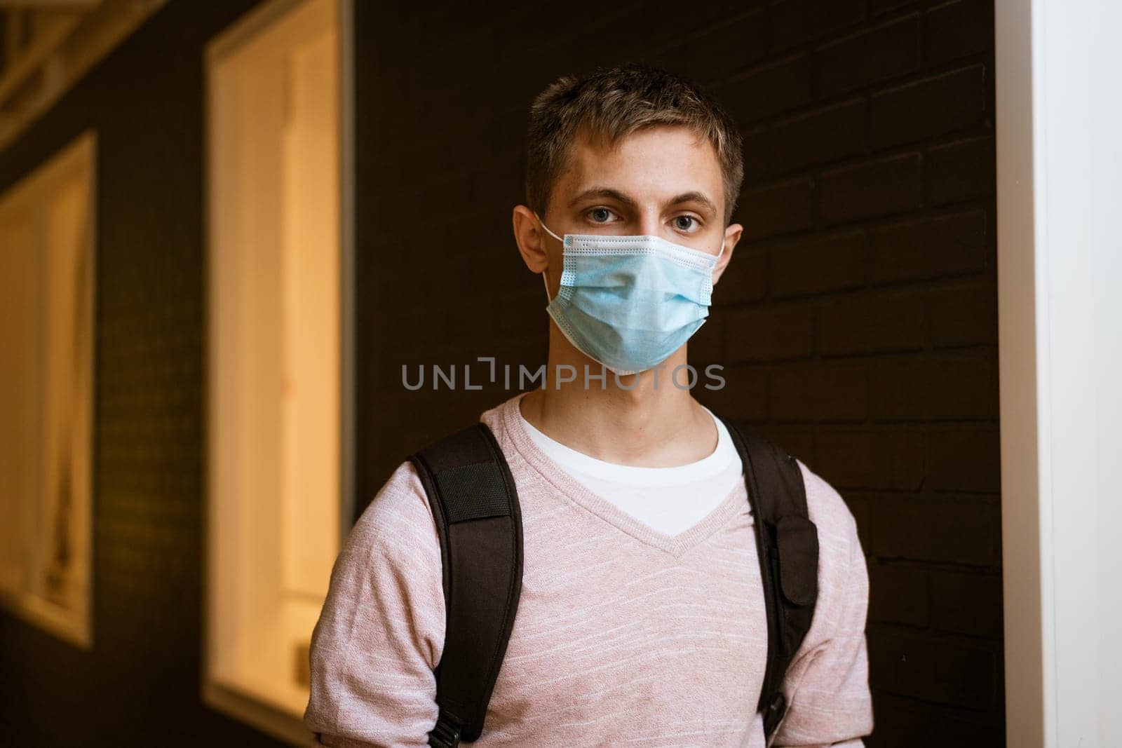 a guy of Caucasian appearance in casual clothes in a protective medical mask with a hands on his back looks at the camera