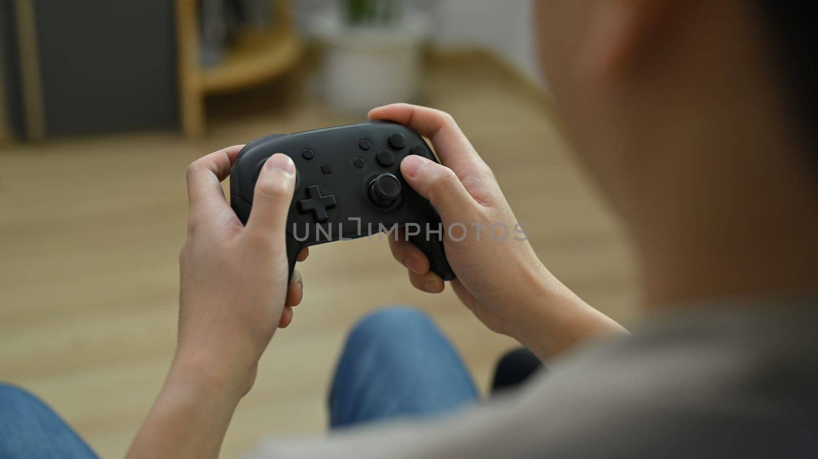 View over shoulder of young man holding wireless controller playing video game. Entertainment, technology and hobby concept by prathanchorruangsak