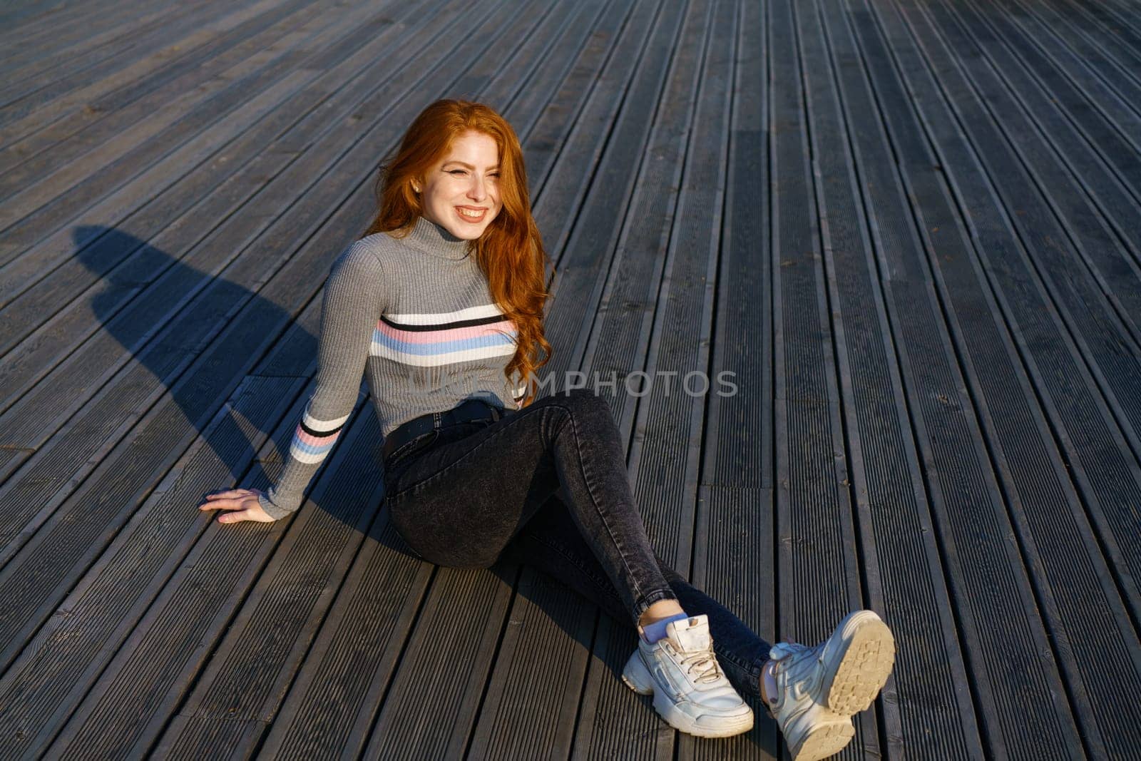 Happy young woman with red hair in the park on wooden flooring by EkaterinaPereslavtseva