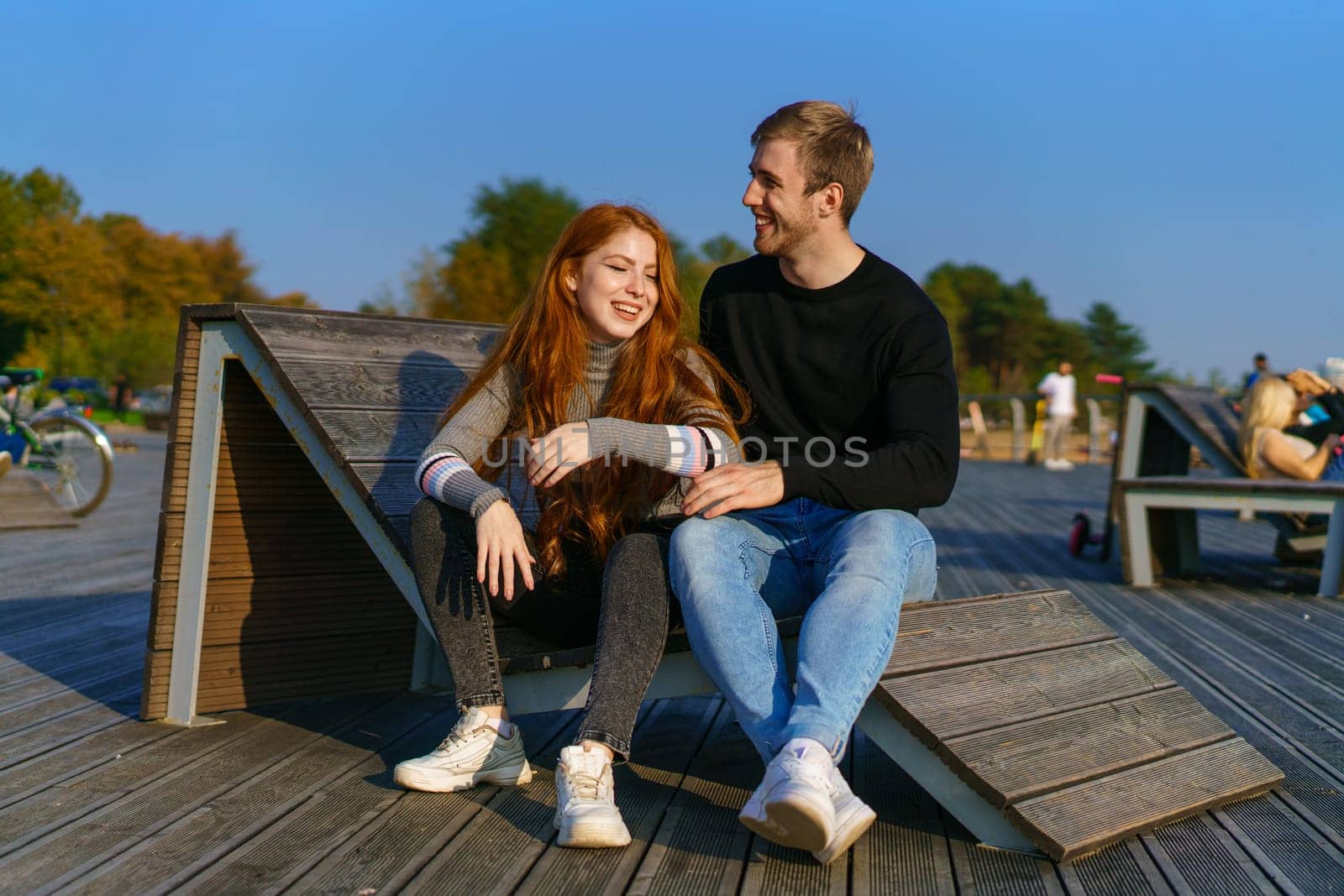 young couple of guy and girl with red hair of Caucasian appearance, in casual clothes, on a sunny day sitting in the park on a wooden bench in an embrace, happy relationship between a man and a woman