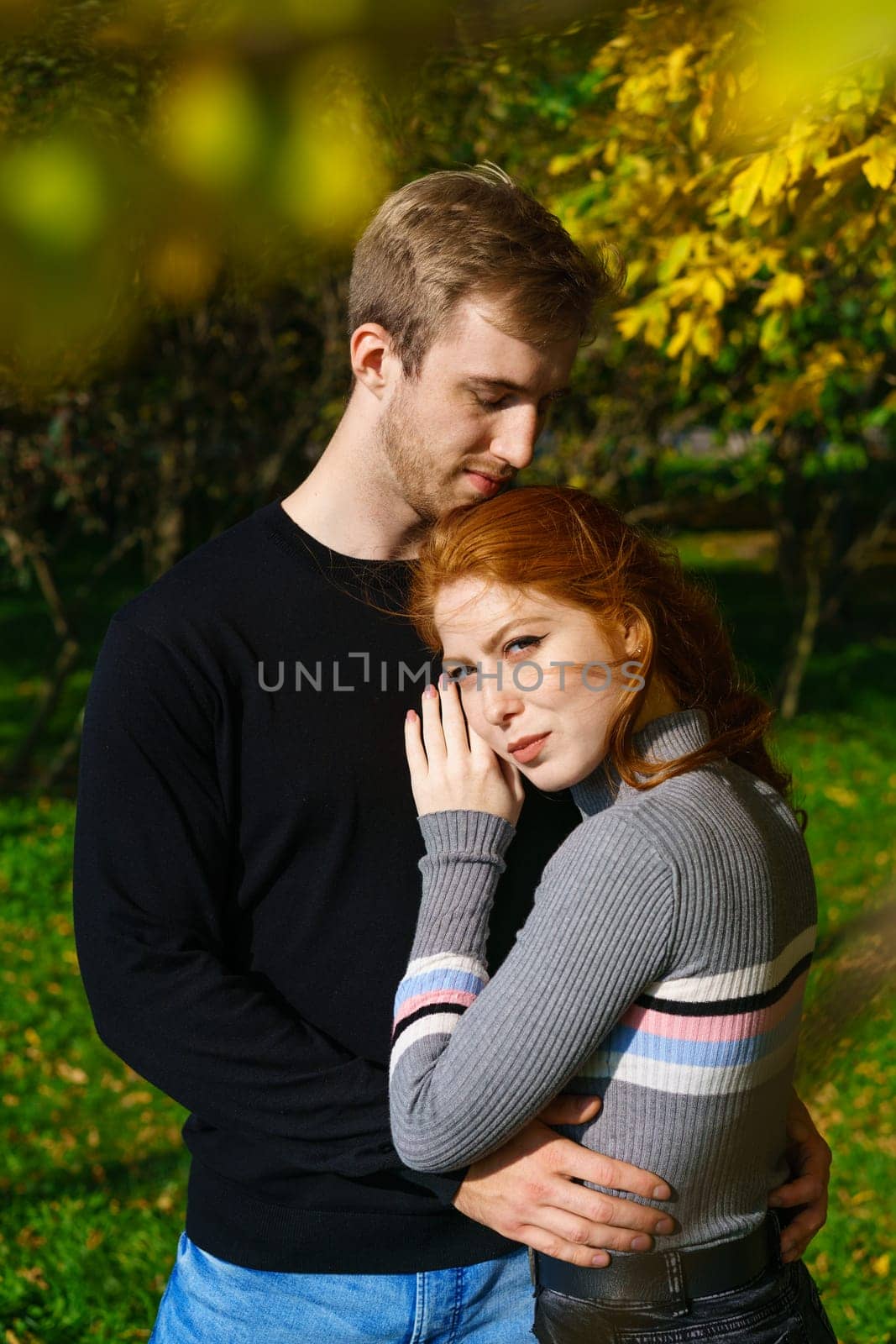 a young couple of Caucasian ethnicity, a man and a woman with red hair are standing in an embrace in a park on a sunny day against the background of trees