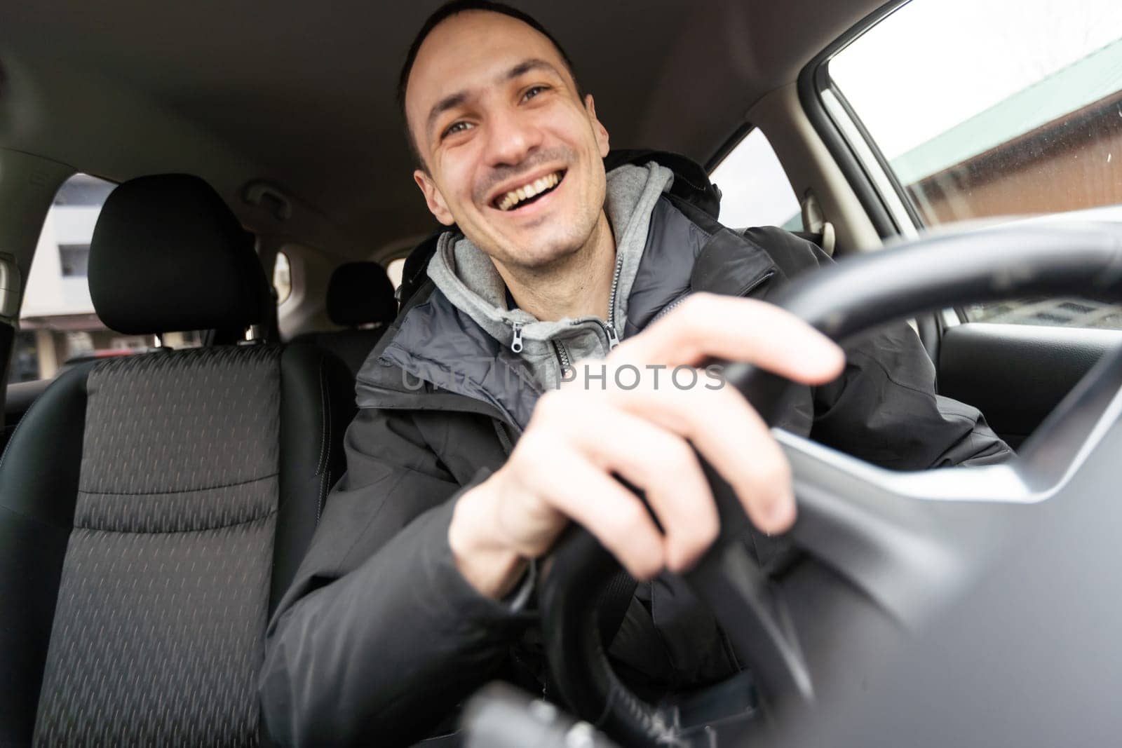 Success in motion. Handsome young man in full suit smiling while driving a car by Andelov13