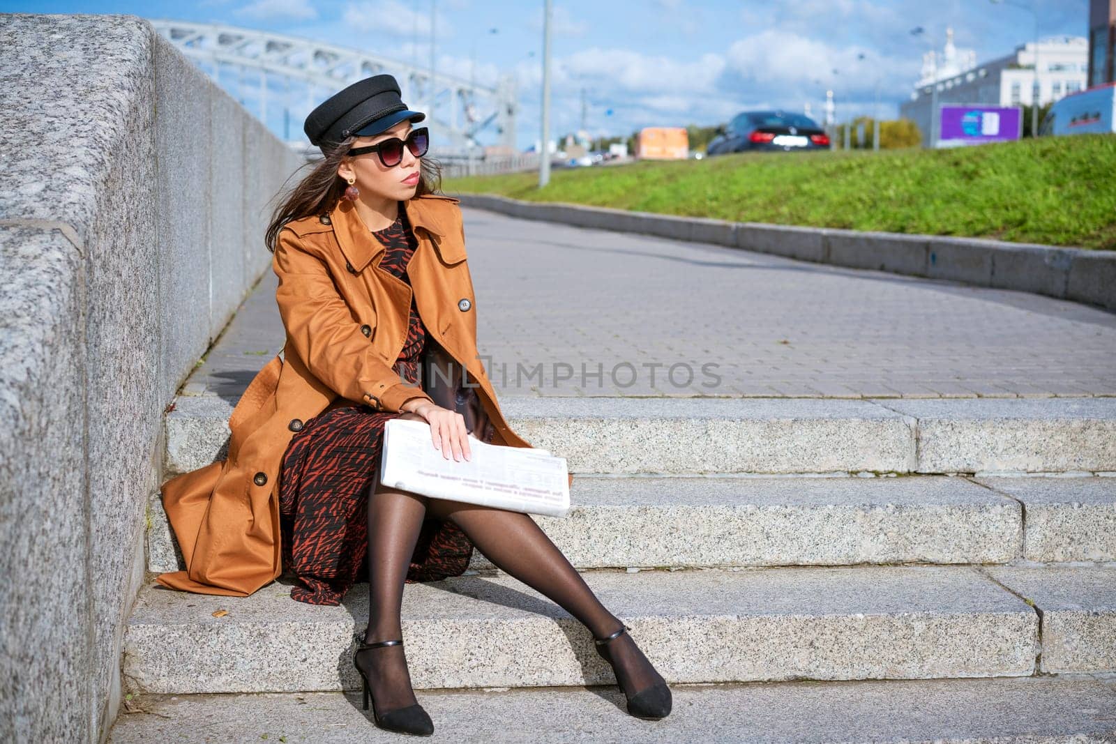 Young woman sits on the steps on the embankment with newspaper in hand by EkaterinaPereslavtseva