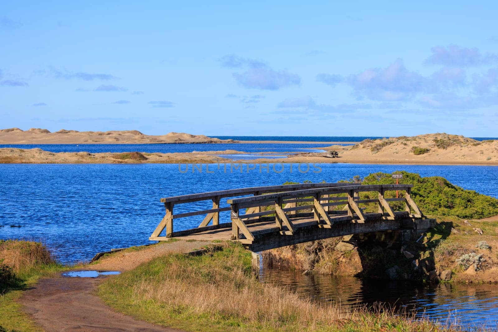 Wooden bridge over blue water in dry sandy landscape on California coast. High quality photo