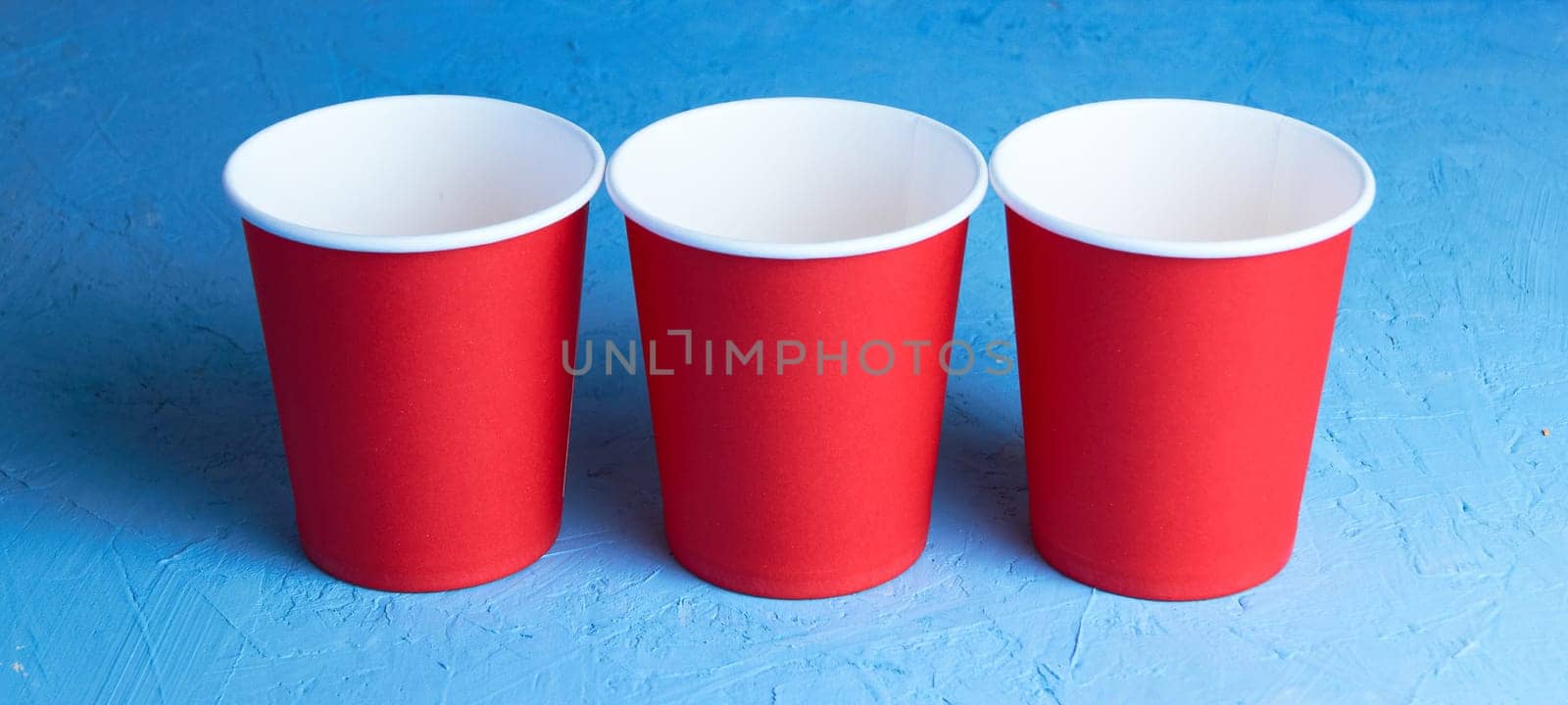 Three red disposable cups on a blue background. Place for text by Севостьянов