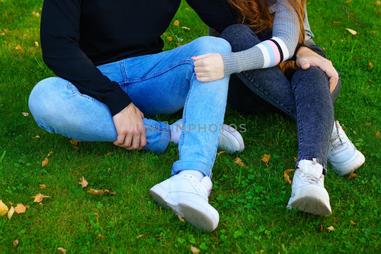 Happy young couple of Caucasian ethnicity man and woman in casual clothes sitting embracing in the park on green grass on a sunny day. Happy relationship between prana and a girl in nature