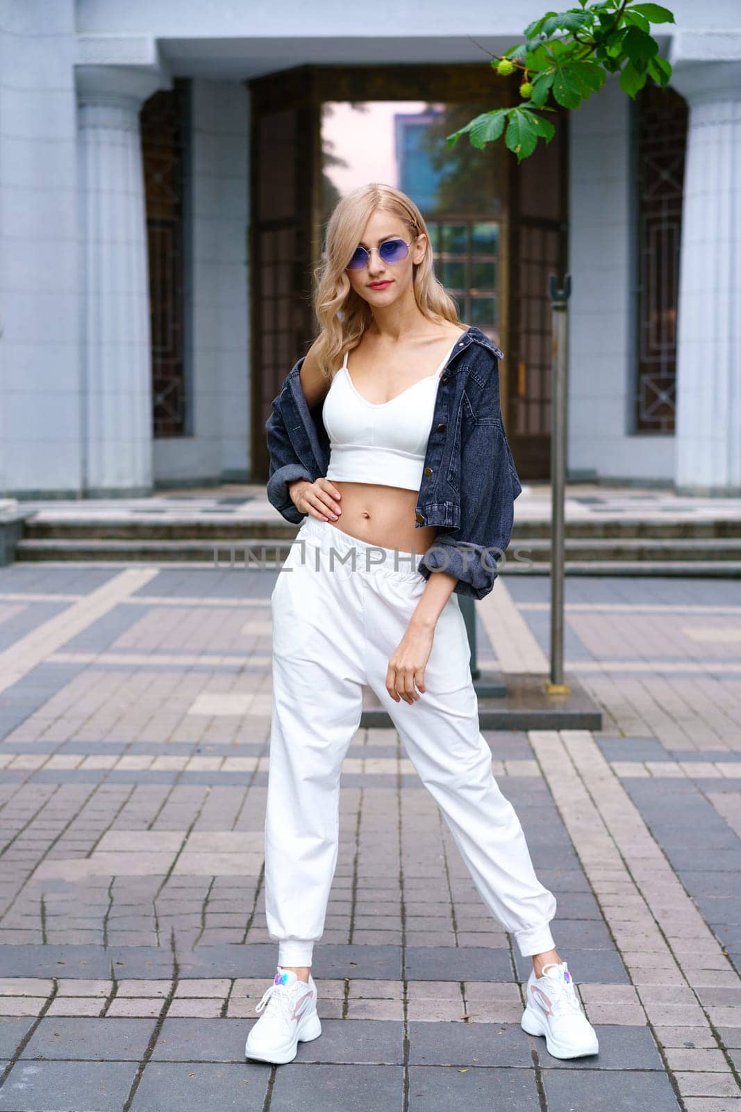 Young woman posing on the street of the city in a tracksuit and sunglasses by EkaterinaPereslavtseva