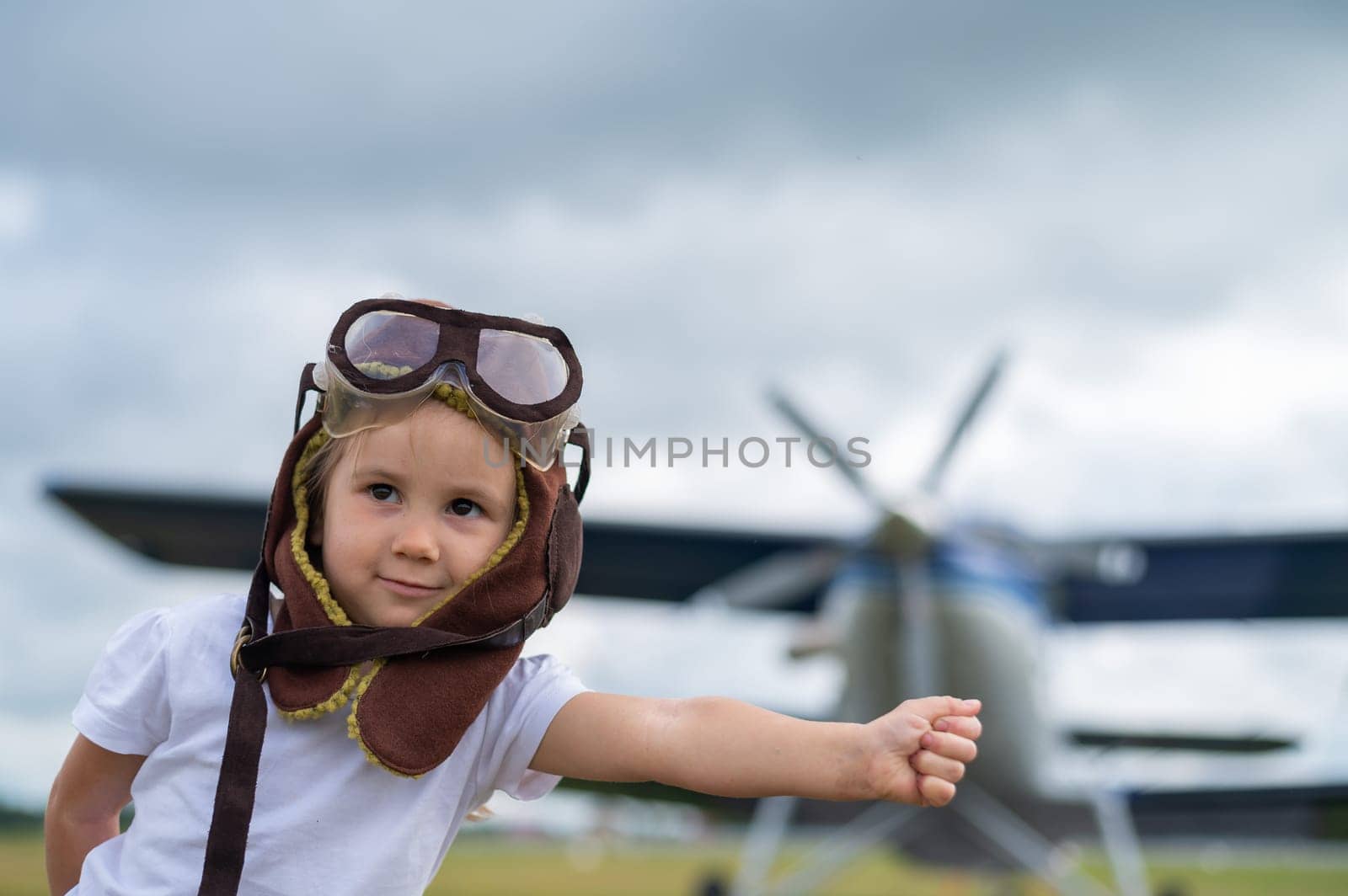 A cute little girl dressed in a cap and glasses of a pilot on the background of an airplane. The child dreams of becoming a pilot. by mrwed54