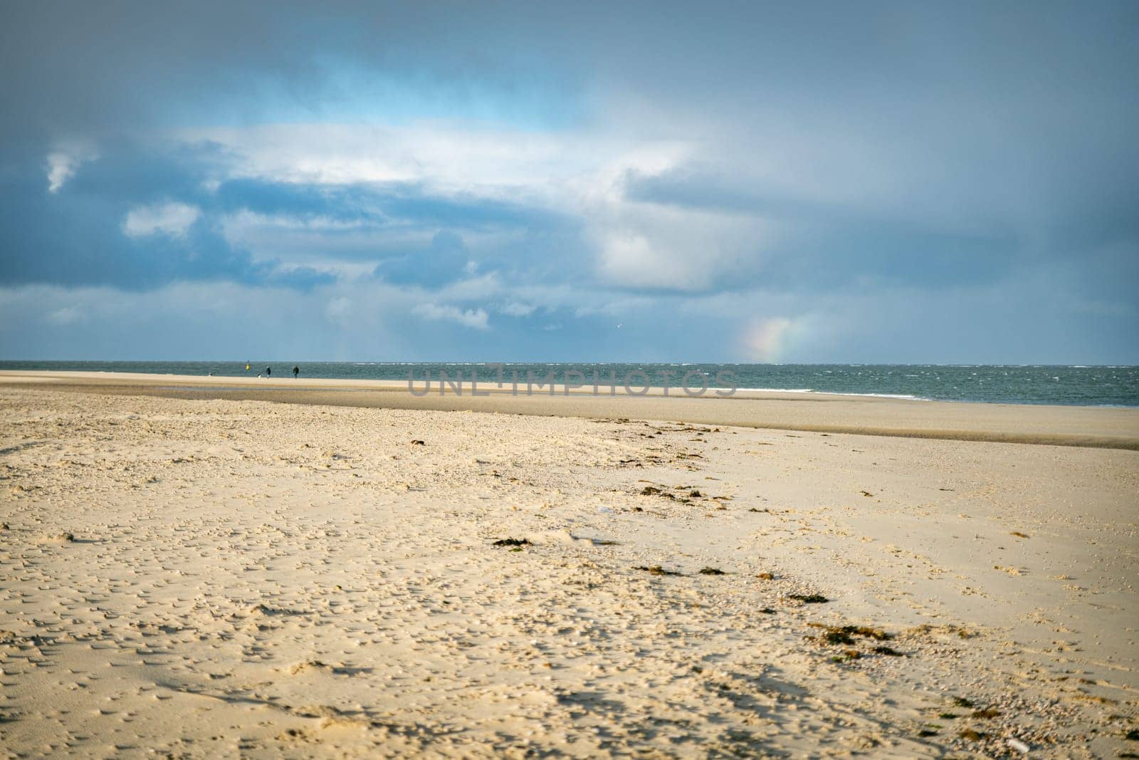 people walking at the beach of the island texel with a small rainbow above the horizon