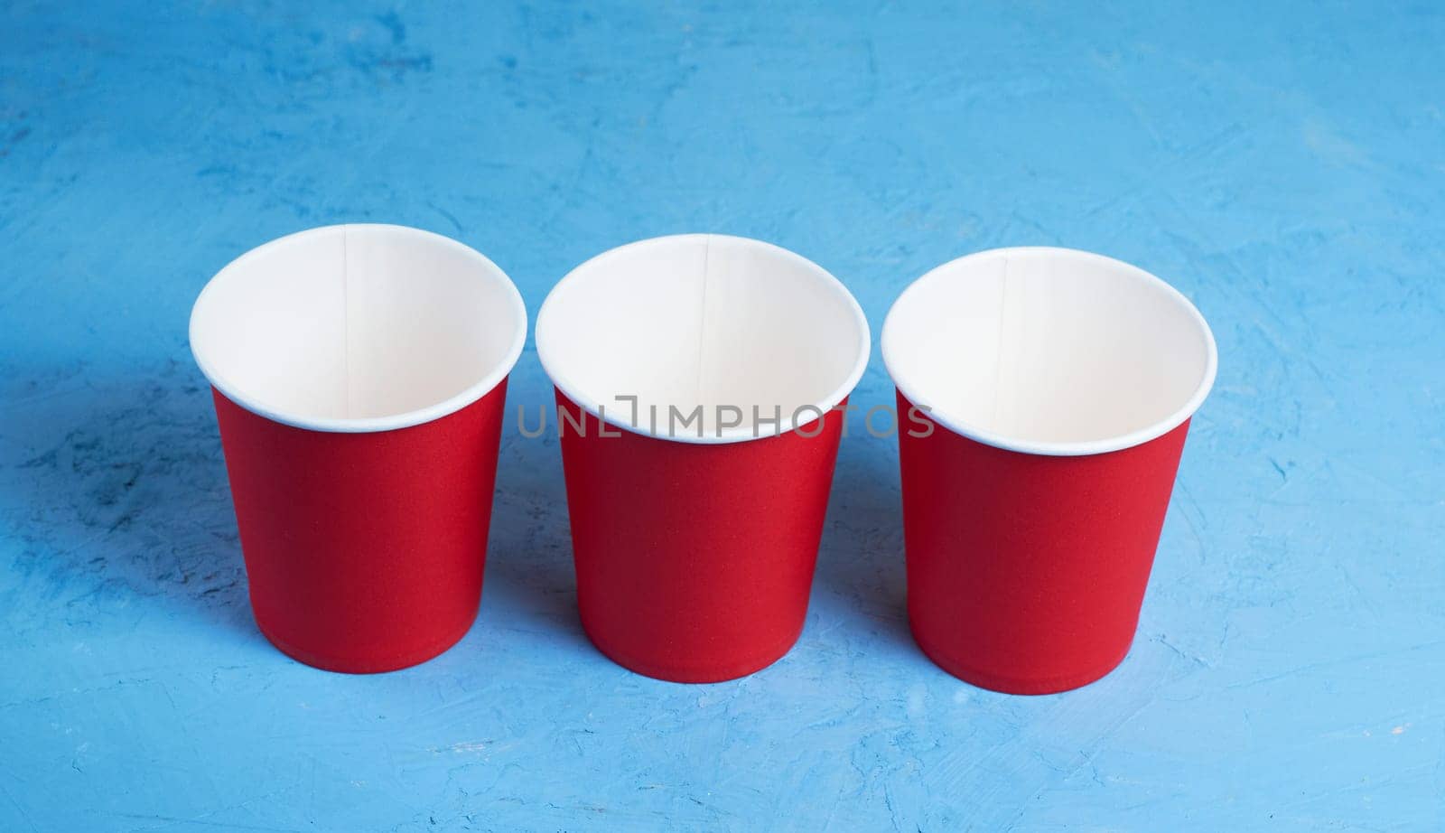 three red paper coffee cups on a blue background with a place to copy the text. Morning concept.