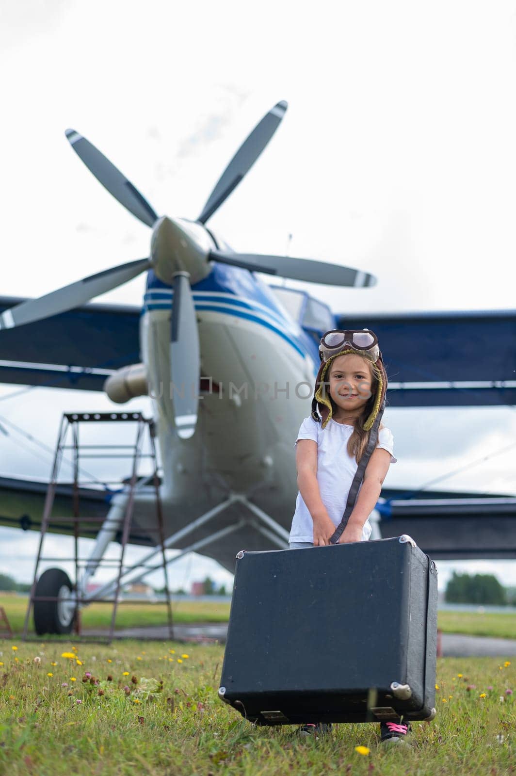 A cute little girl playing on the field by private jet dreaming of becoming a pilot.