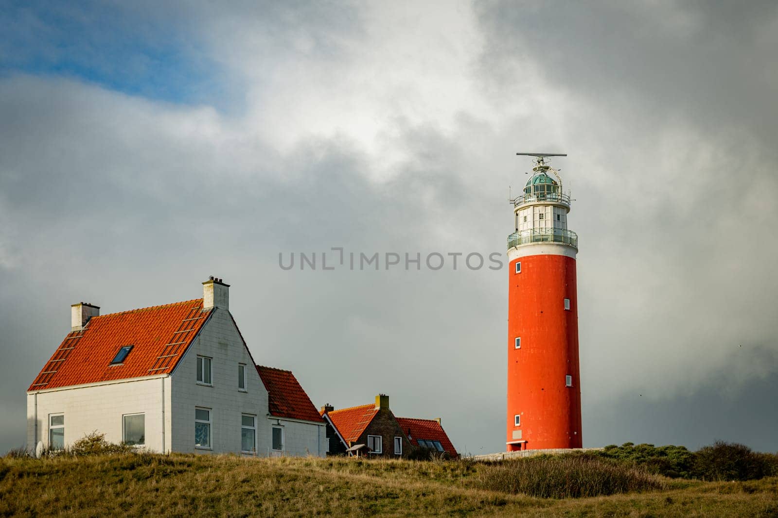 Red lighthouse at the little isle of Texel, the Netherlands with small small old red h and white houses by compuinfoto