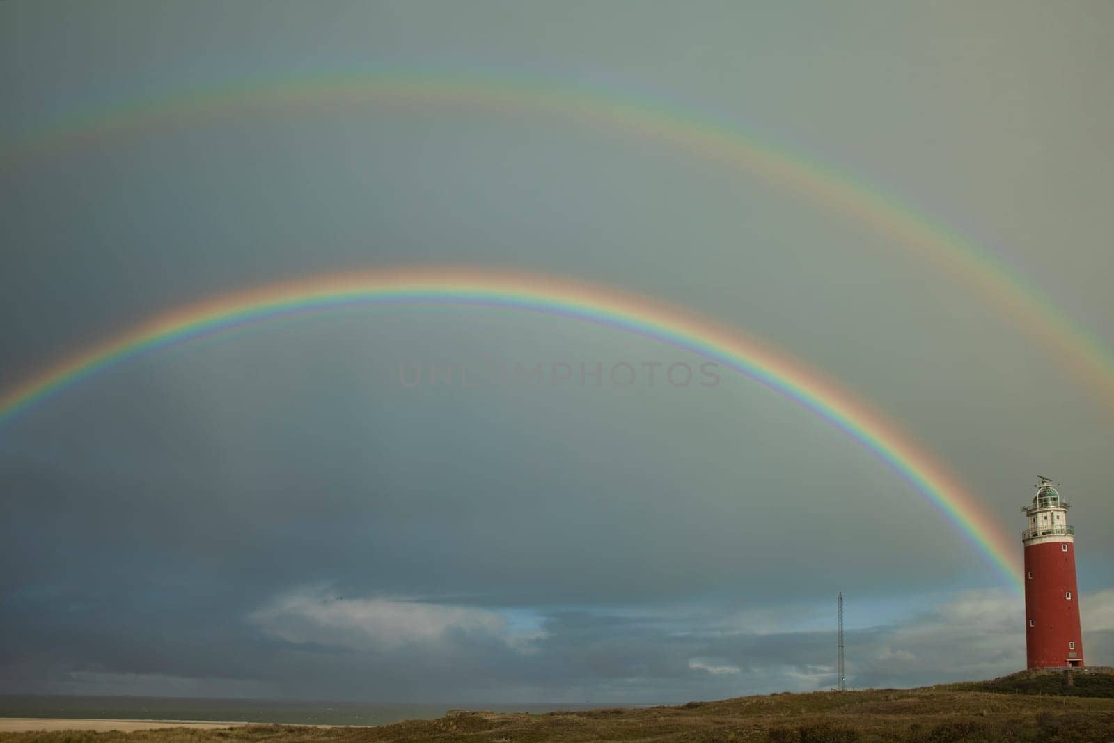 the lighthouse of the island of Texel with a double rainbow above the sea and the dunes in the background