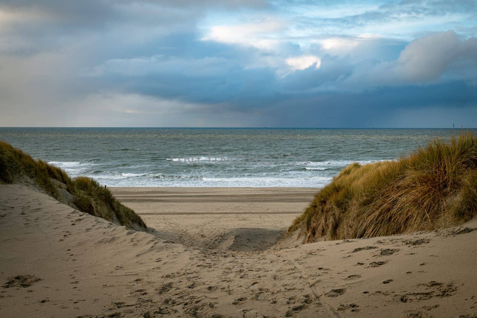 the access to the beach at the top on the island of Texel in the Netherlands with the dunes with the horizon and the dark clouds in the background