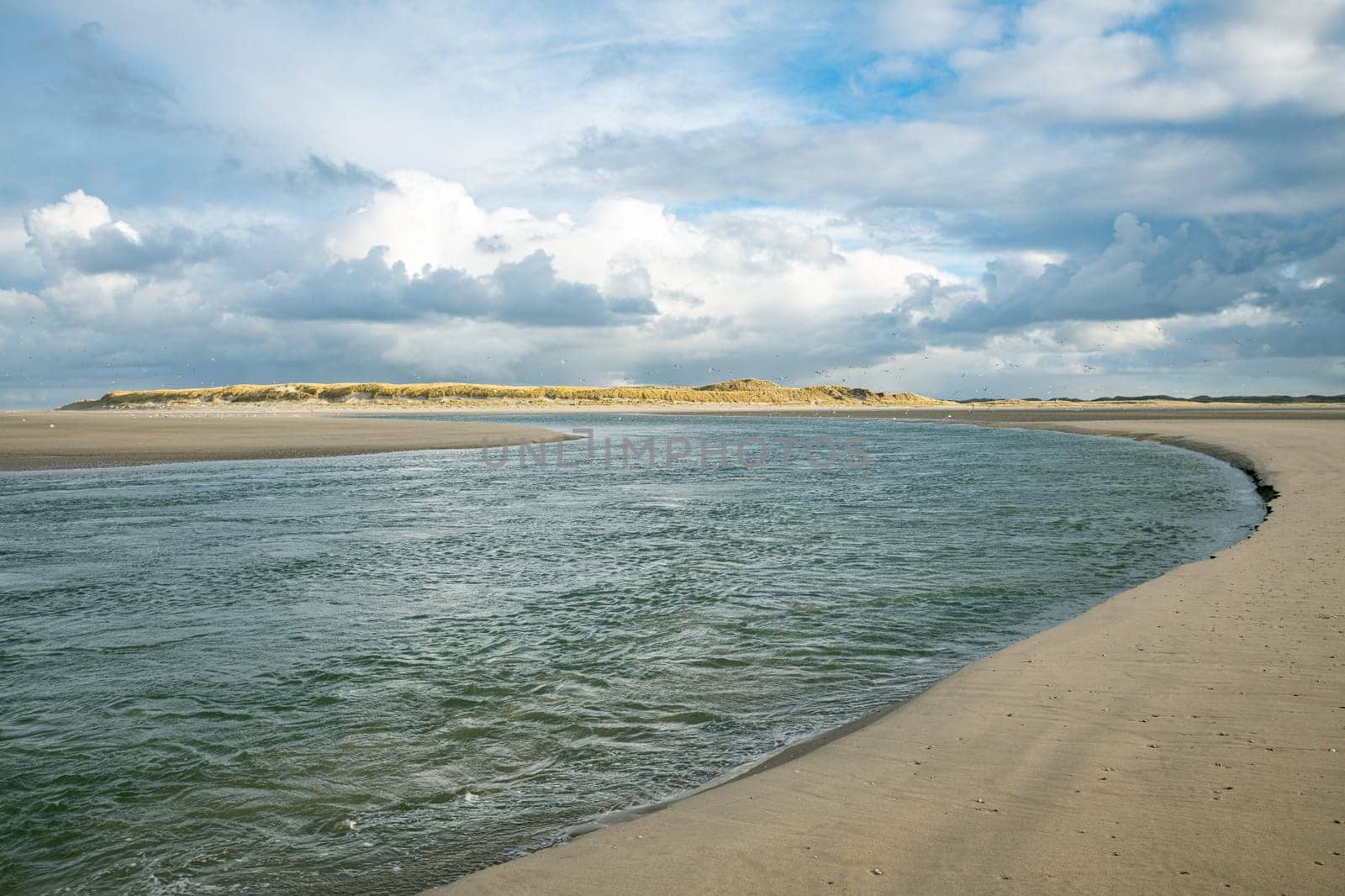 a stretch of beach by the sea with the sun on the dunes in the background of the island of Texel in the Netherlands