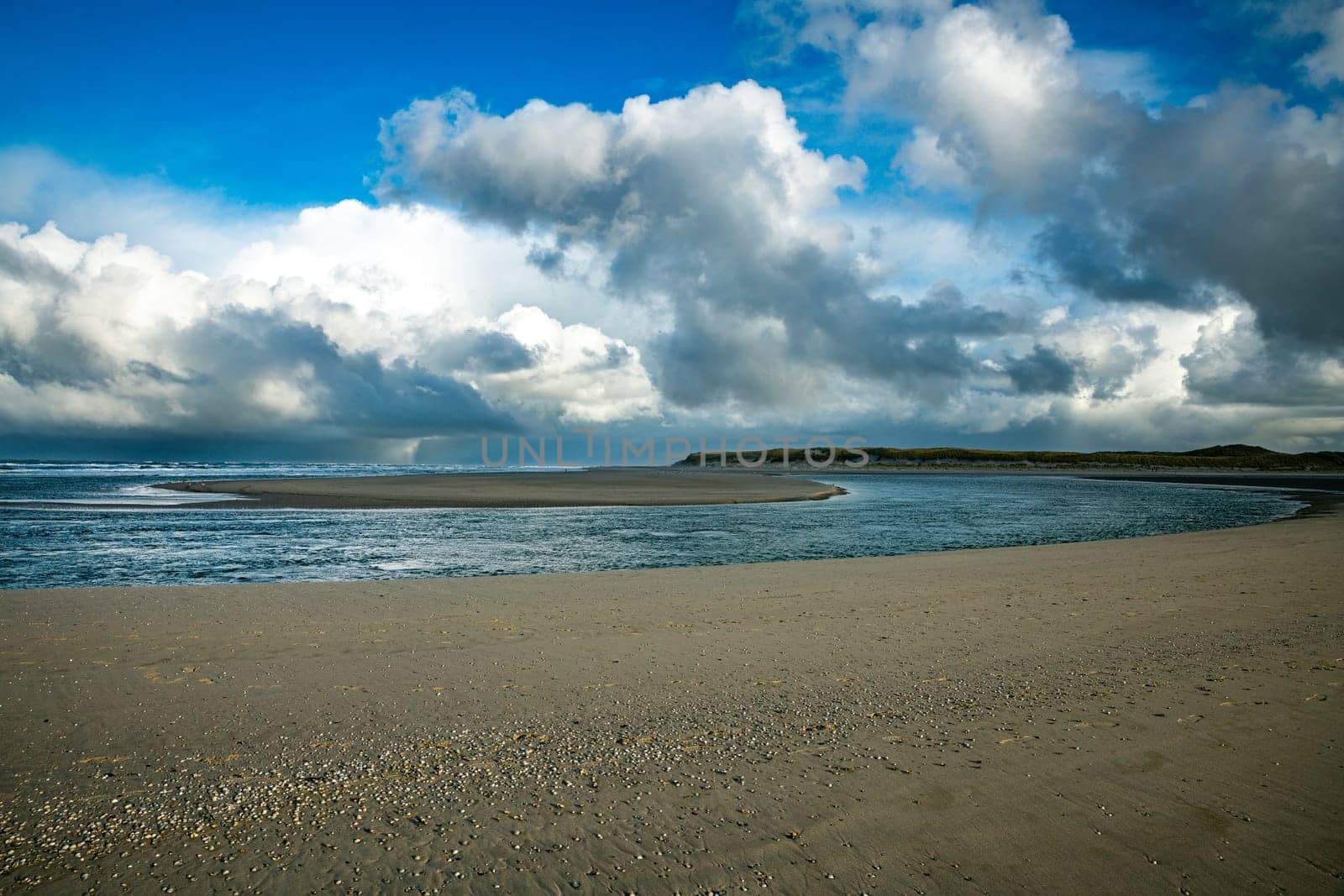 the beach of the island of Texel with dark clouds in the background and a cove with a sandbar in the middel