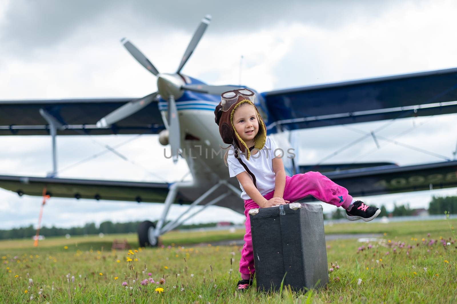 A cute little girl playing on the field by a four-seater private jet dreaming of becoming a pilot.