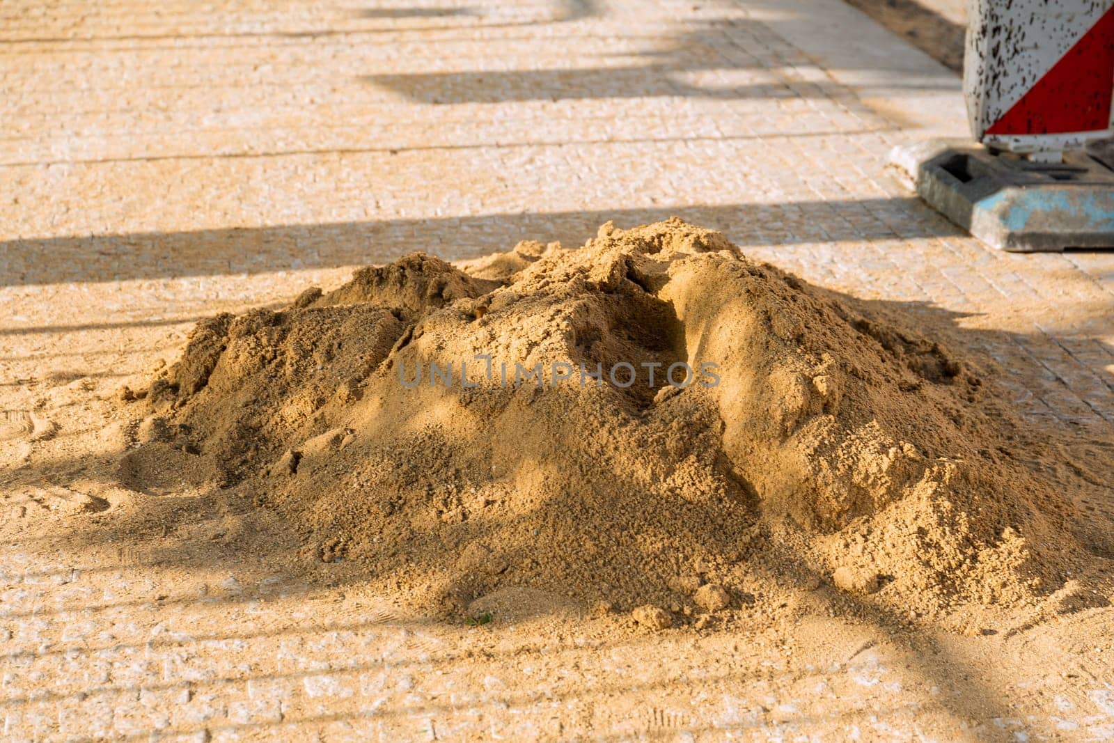 A pile of sand for filling the joints between paving stones. Laying paving stones on sand. Installation of new sidewalks. Road construction works in the city.