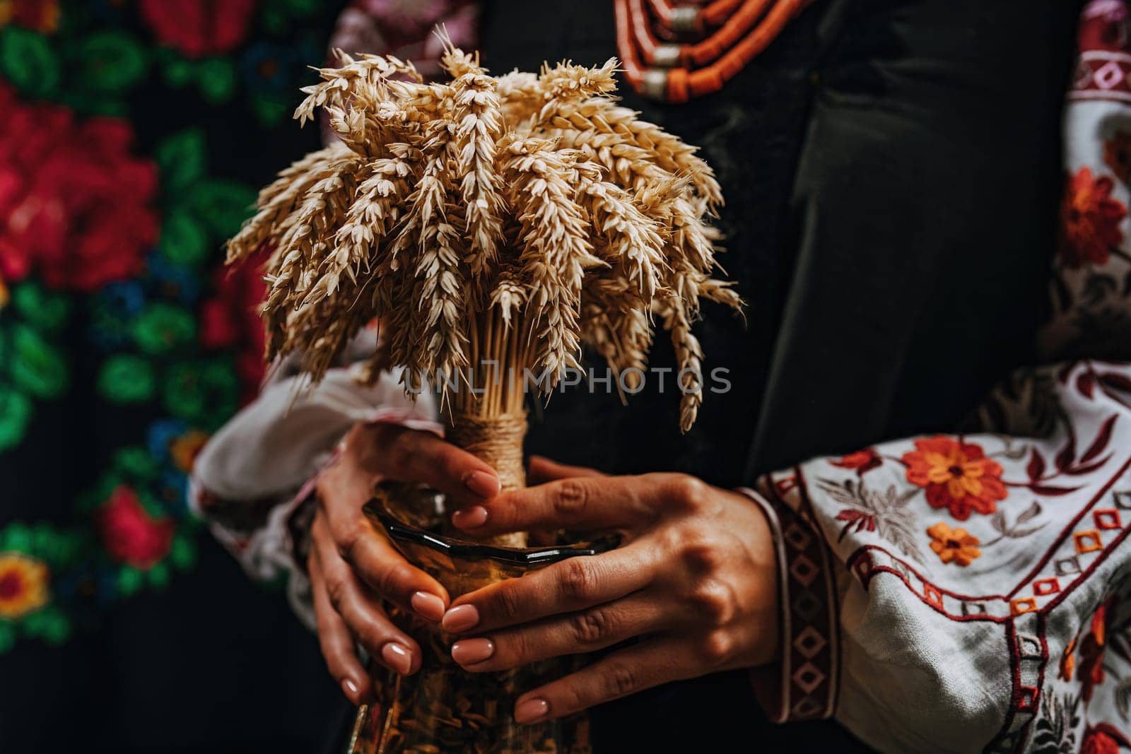 Ukrainian woman in traditional costume with bouquet Didukh on colorful bukovyna ornaments carpet. Christmas decoration, made from sheaf of wheat.