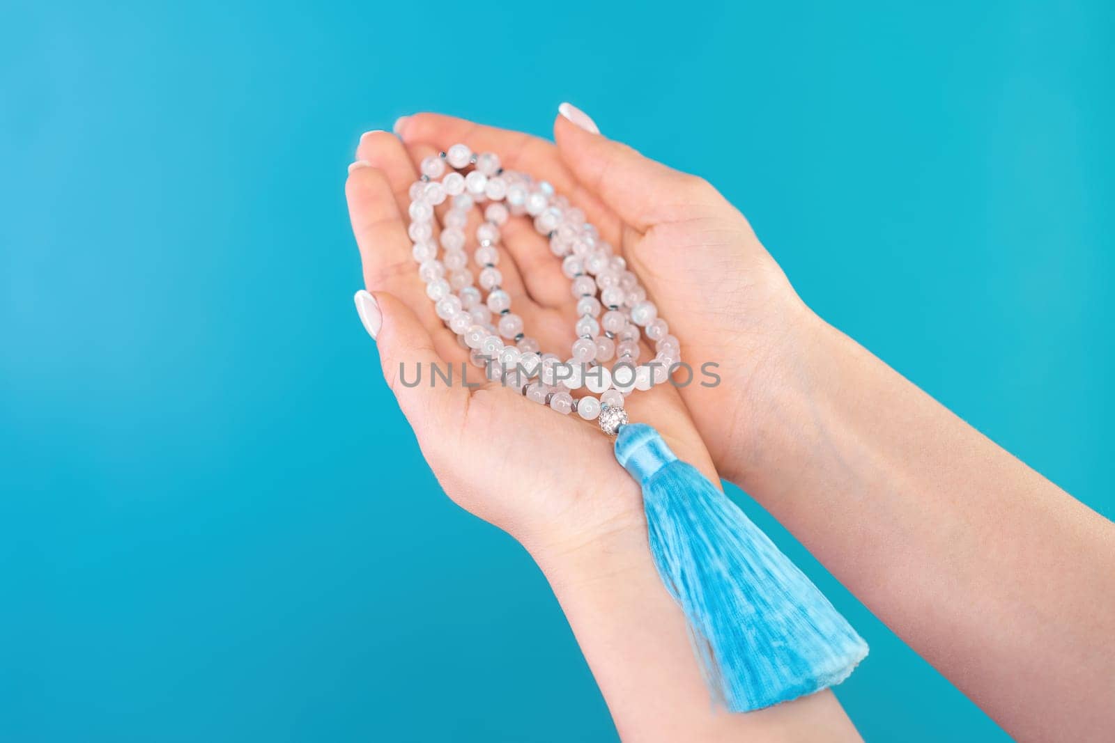 Moon stone mala beads in female hand on blue background. Gemstone strand used for keeping count during mantra meditations. Spirituality, religion, God concept.