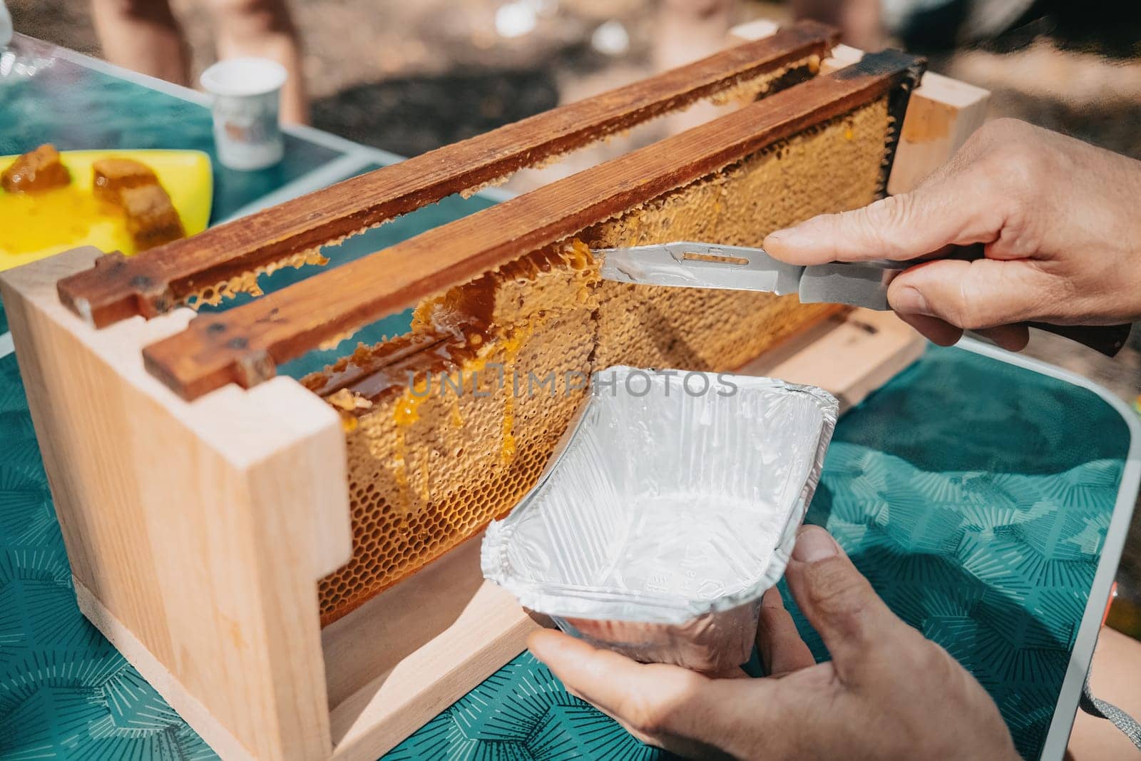 Knife cuts off sealed honeycomb and sweet honey flows out of it. Production of nectar in apiary. Manual labor, insect care. Beekeeping culture concept, yellow harvest.