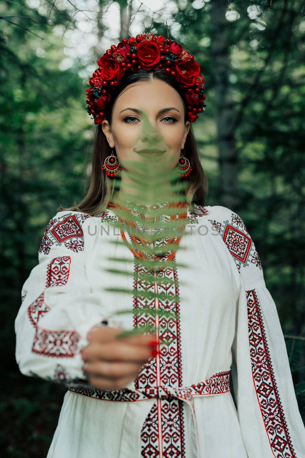 Portrait of ukrainian woman with fern in Carpathian mountains forest. She in in traditional ukrainian wreath, national dress - vyshyvanka, ancient coral beads.