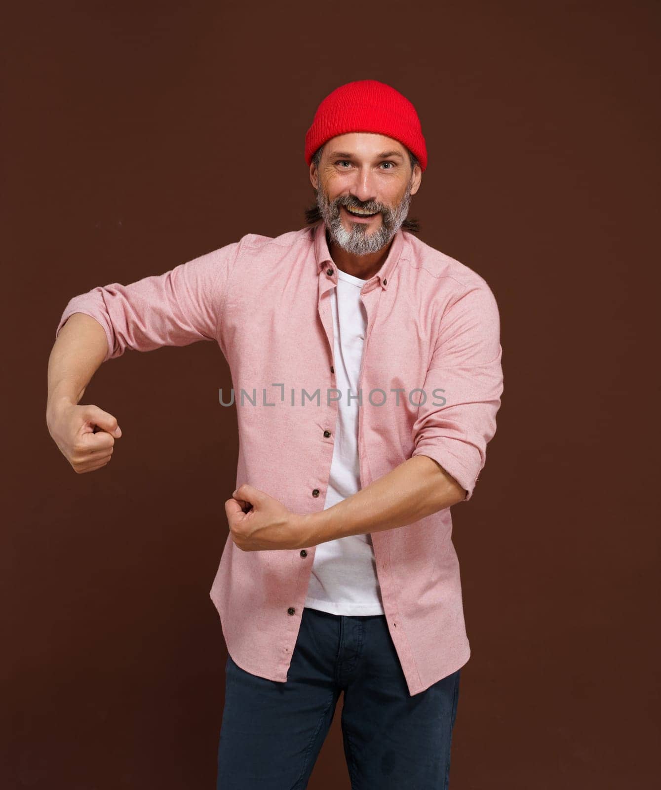 Mature handsome concept. Show strength. middle-aged European man with gray beard showcases his physical strength by flexing his biceps and clenching his fists, exuding confidence and determination. by LipikStockMedia