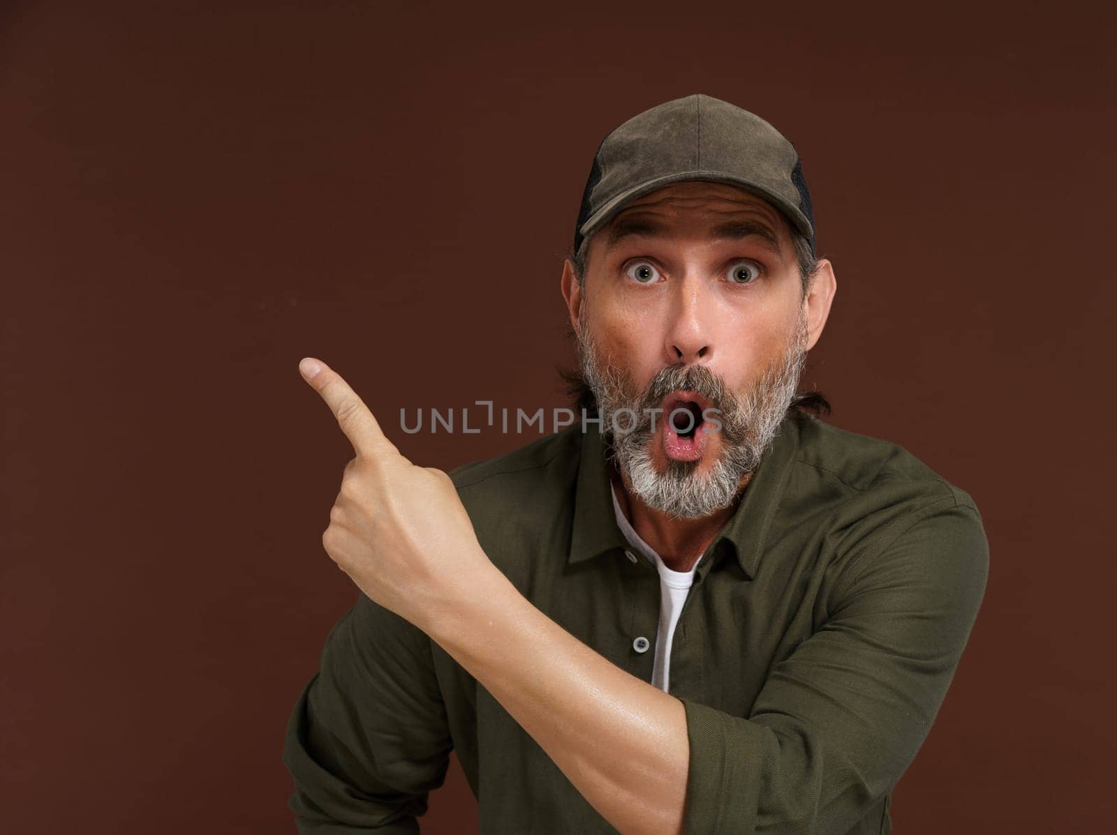 Middle-aged Caucasian country man expresses extreme surprise, pointing his finger to the side. Copy space. Advertising concept. High quality photo