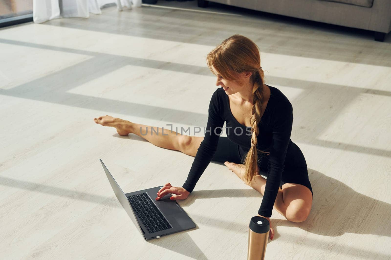 Silver colored laptop. Woman in sportive clothes doing yoga indoors.