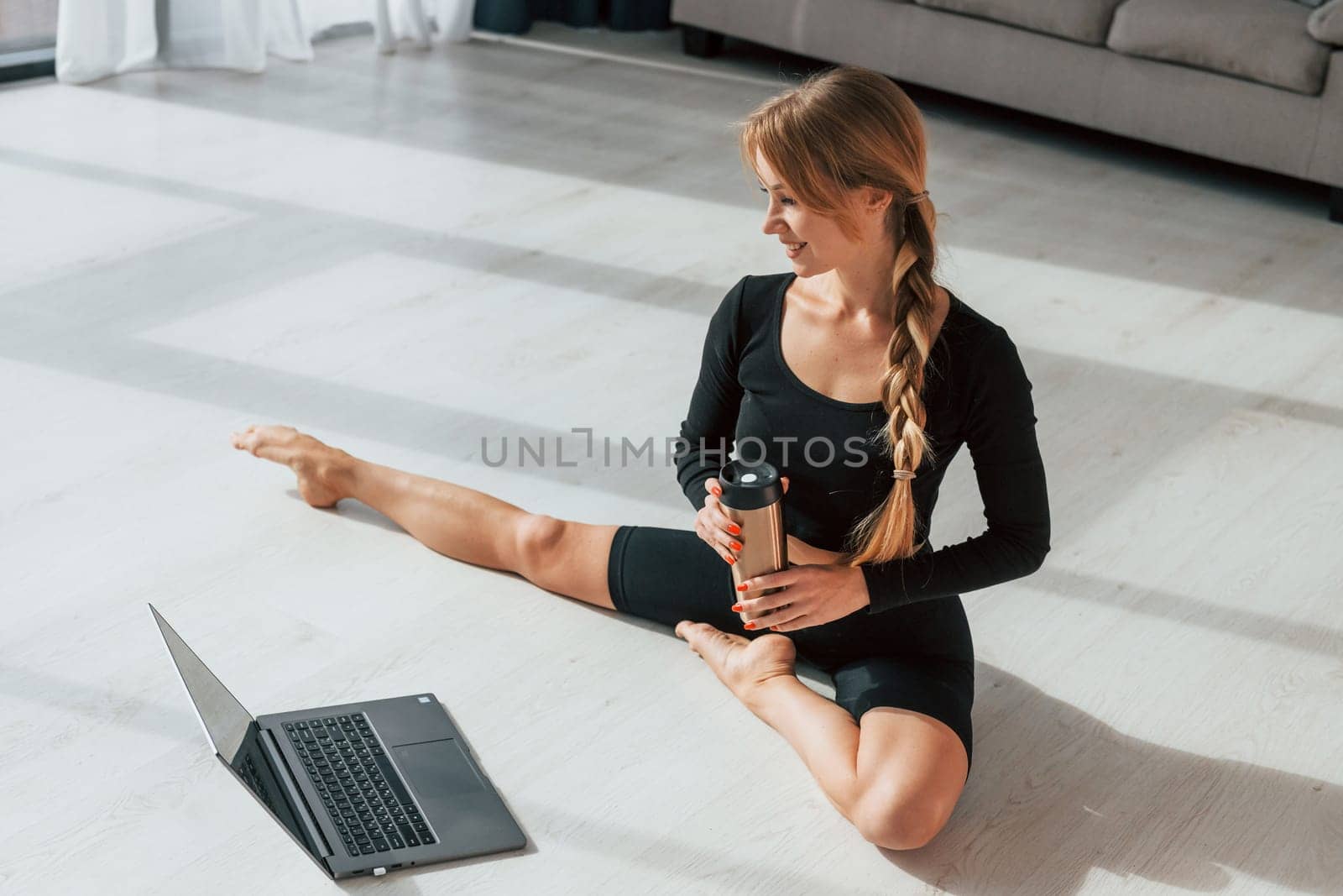 Silver colored laptop. Woman in sportive clothes doing yoga indoors.