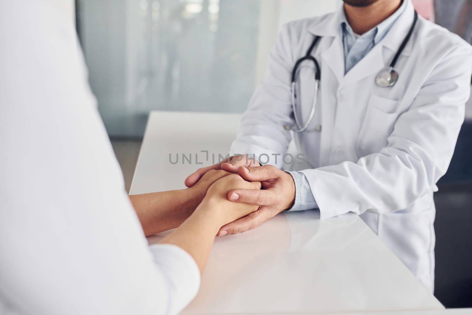 Holding customer by the hands. Professional medic in white coat is in the clinic.