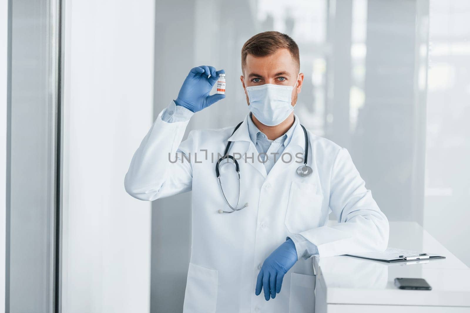 In blue gloves. Professional medic in white coat is in the clinic by Standret